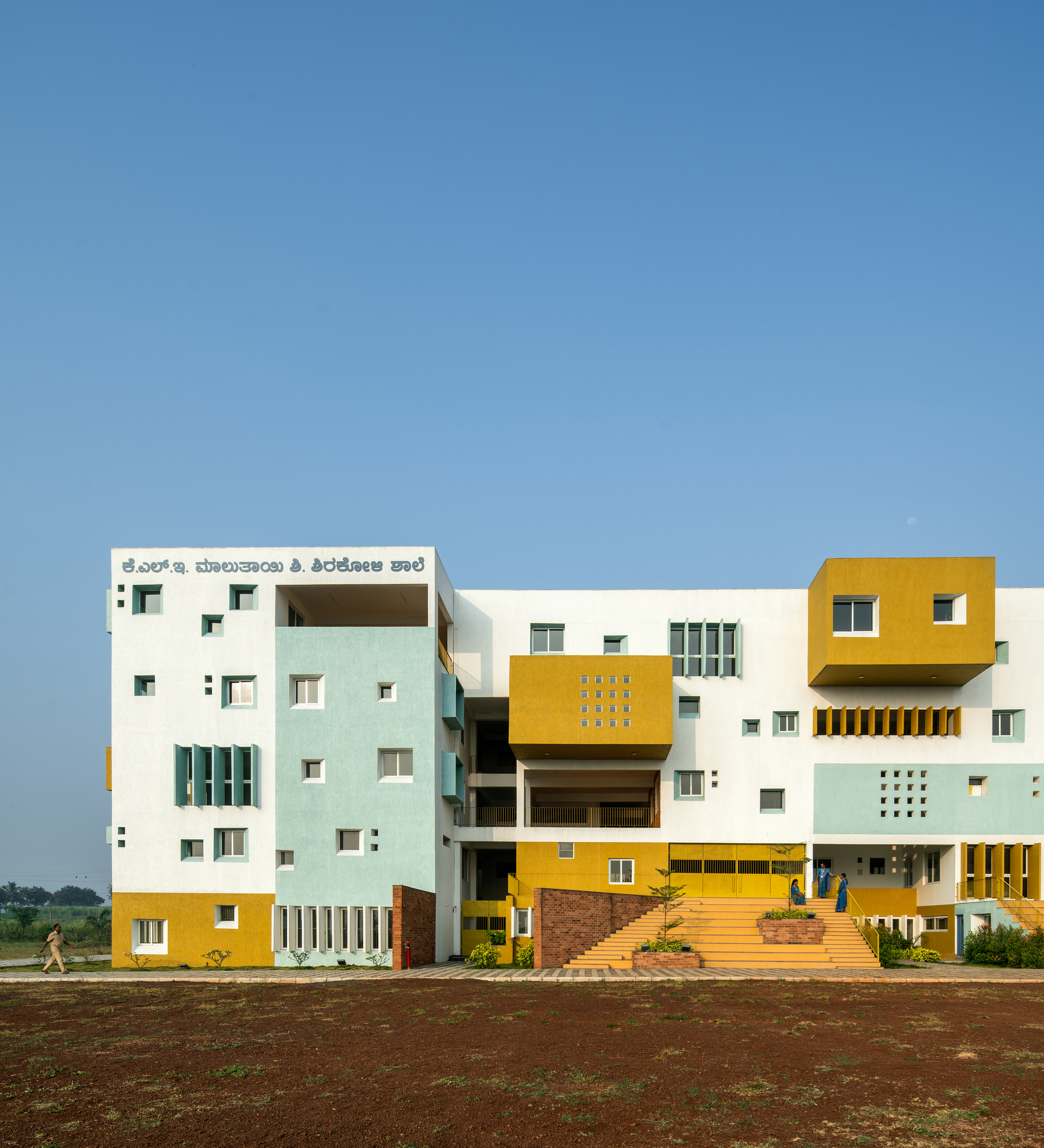 Front elevation showing stacked volumes in white, yellow and pale blue with cantilevered upper floors under clear sky