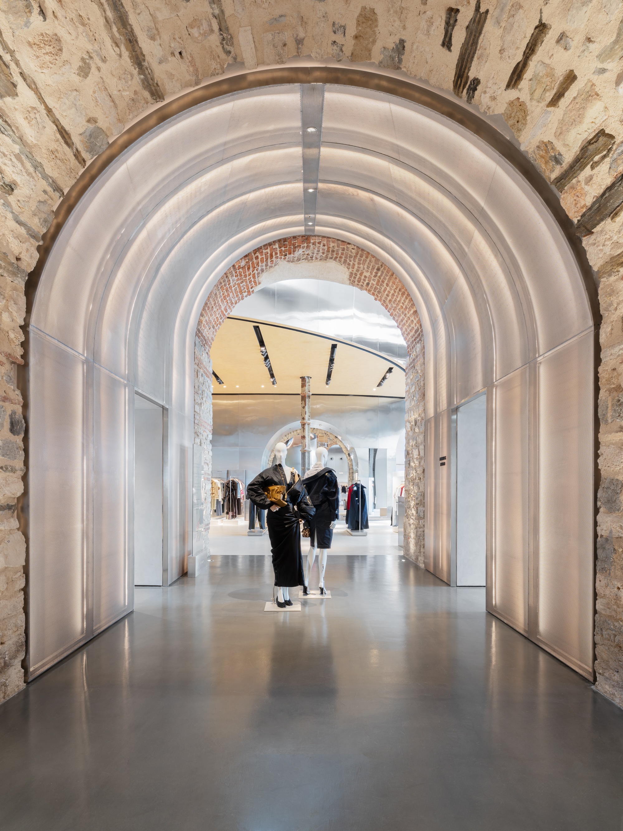 Polished metal arched passageway framing a sequence of vaults and shoppers in the retail gallery beyond