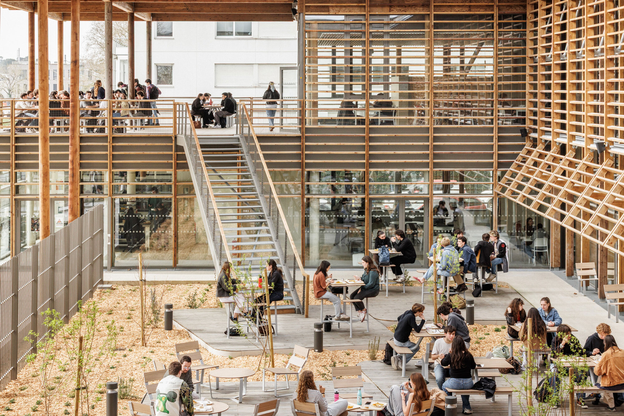 Ground-level view of the courtyard filled with visitors at tables beneath timber staircases and lattice walls