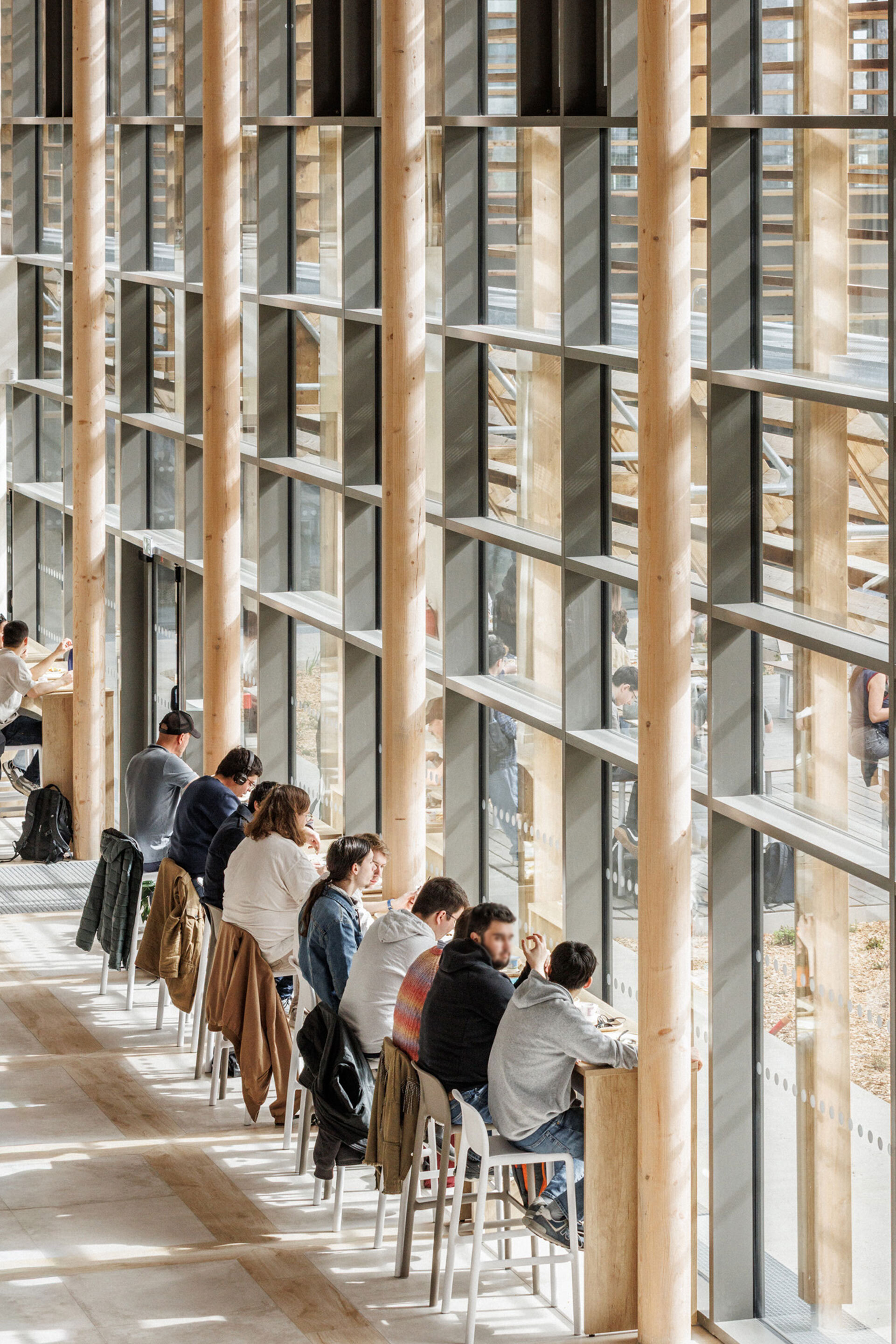 Window counter lined with visitors seated on stools between vertical timber mullions and glass panels