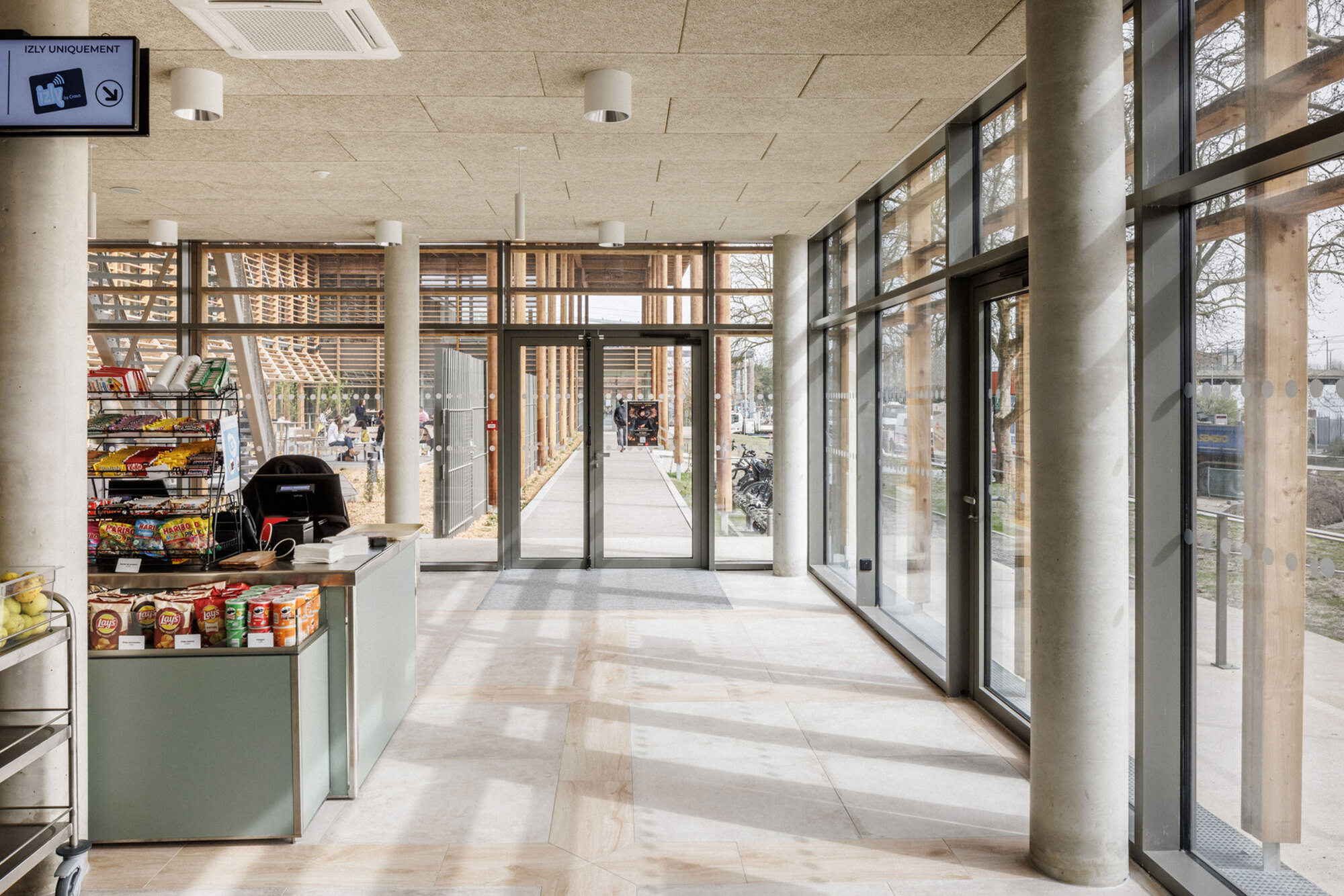 Entrance lobby with cylindrical concrete columns and floor-to-ceiling glazing framed by timber brise-soleil