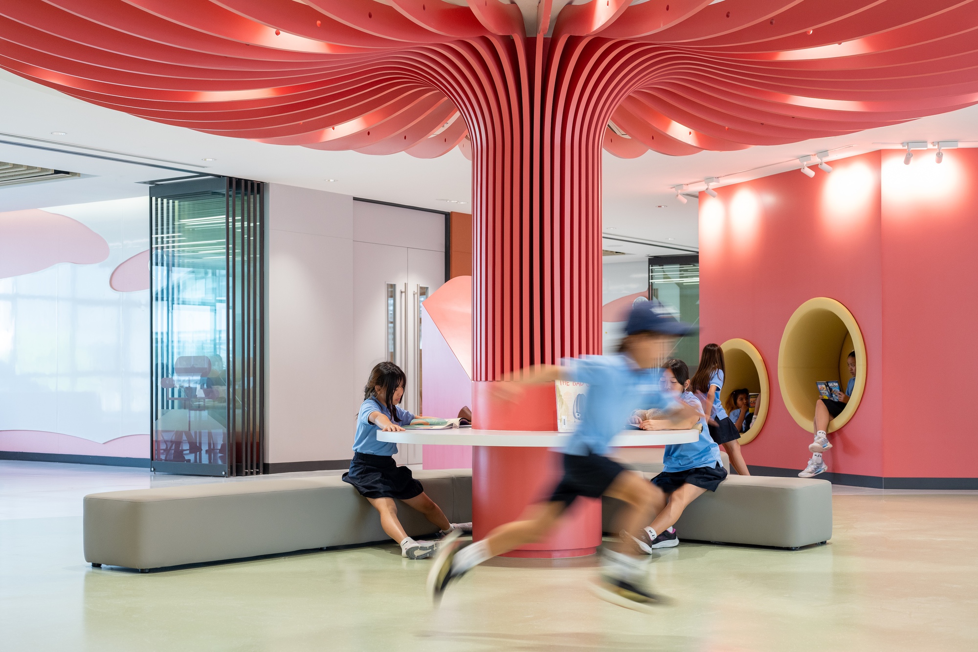 Interior common area with coral-red ribbed column branching into ceiling waves as students move through the space