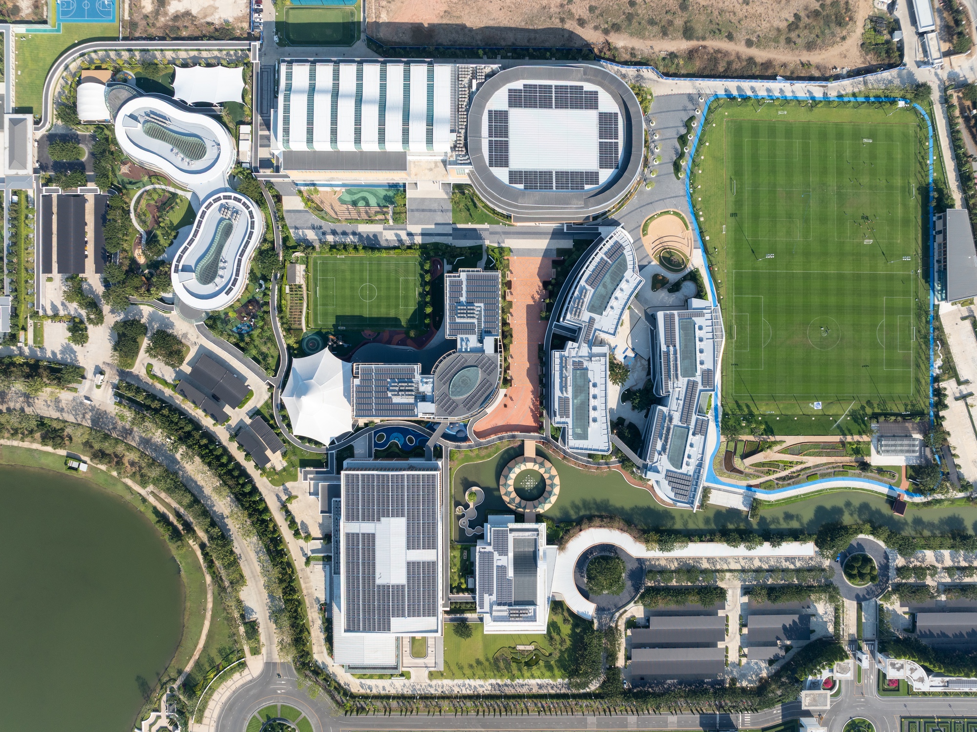 Aerial view of the campus showing circular and curved building footprints amid playing fields and waterfront landscape