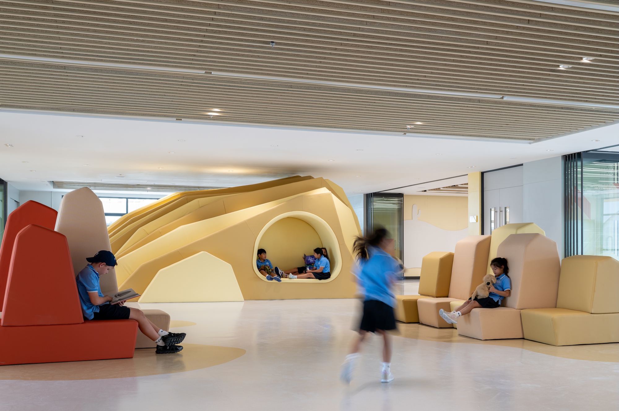 Sculptural yellow foam seating landscape with arched nooks occupied by students in a naturally lit corridor