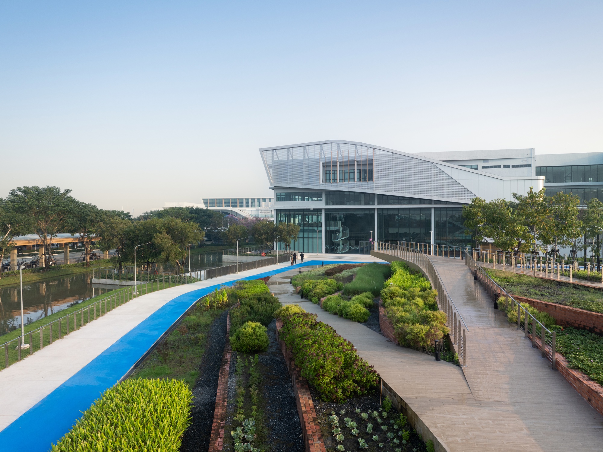 Glass and metal facade with sloping roof above curving pathways and terraced planted beds at dusk