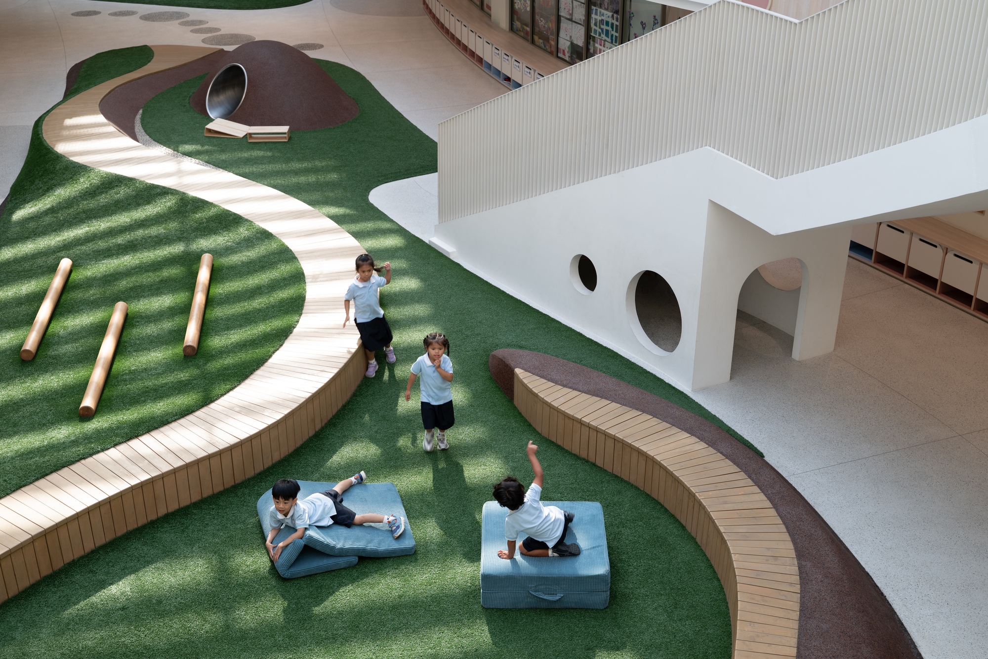 Curved timber-edged pathway winding through artificial turf with children playing and white portal openings