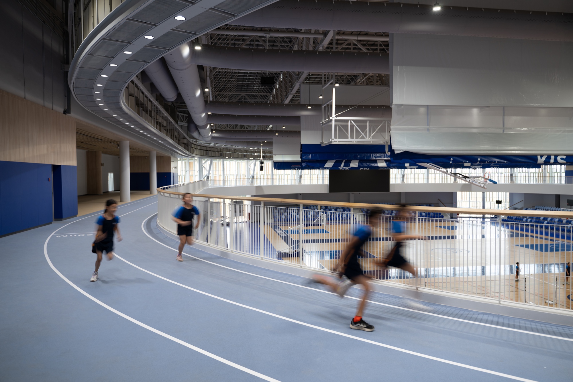 Indoor running track with students in motion under curved ceiling panels and exposed mechanical systems