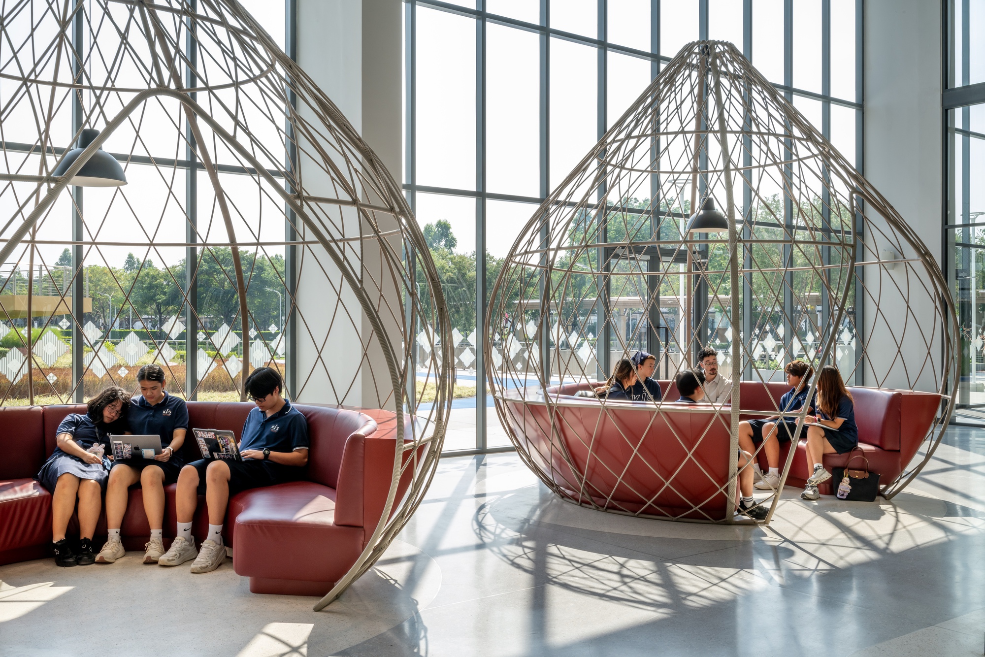 Wireframe pod seating with coral upholstery in a glass-walled lobby with students reading and conversing