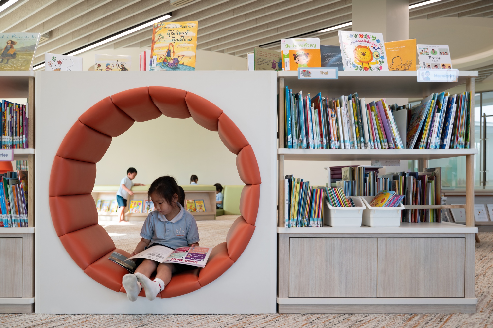 Circular padded reading nook set into white bookshelf partition with child seated inside holding a book