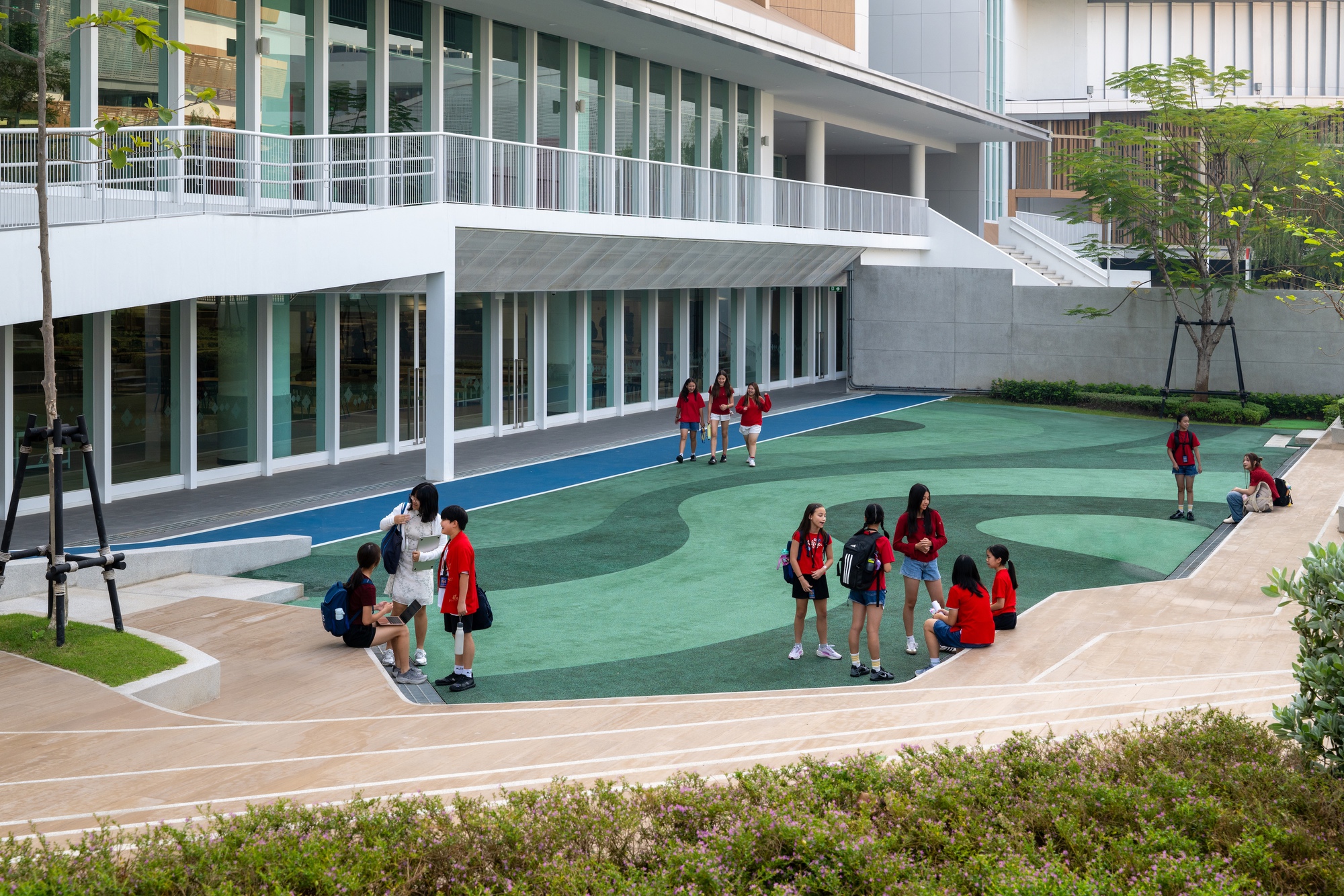 Outdoor courtyard with curving green play surface surrounded by glazed facades and planted edges