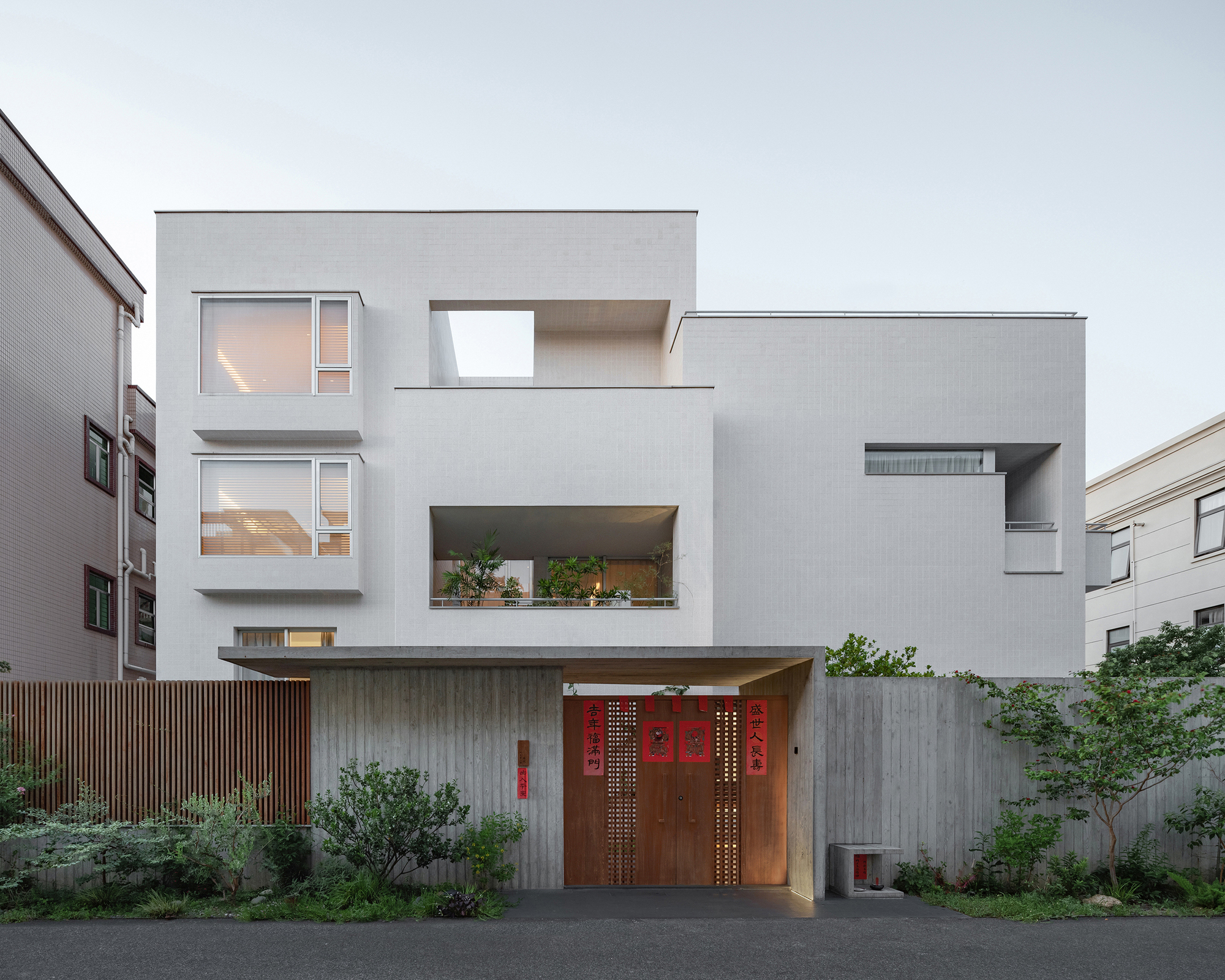 Street view showing the layered white volumes with recessed balconies and timber entry gate
