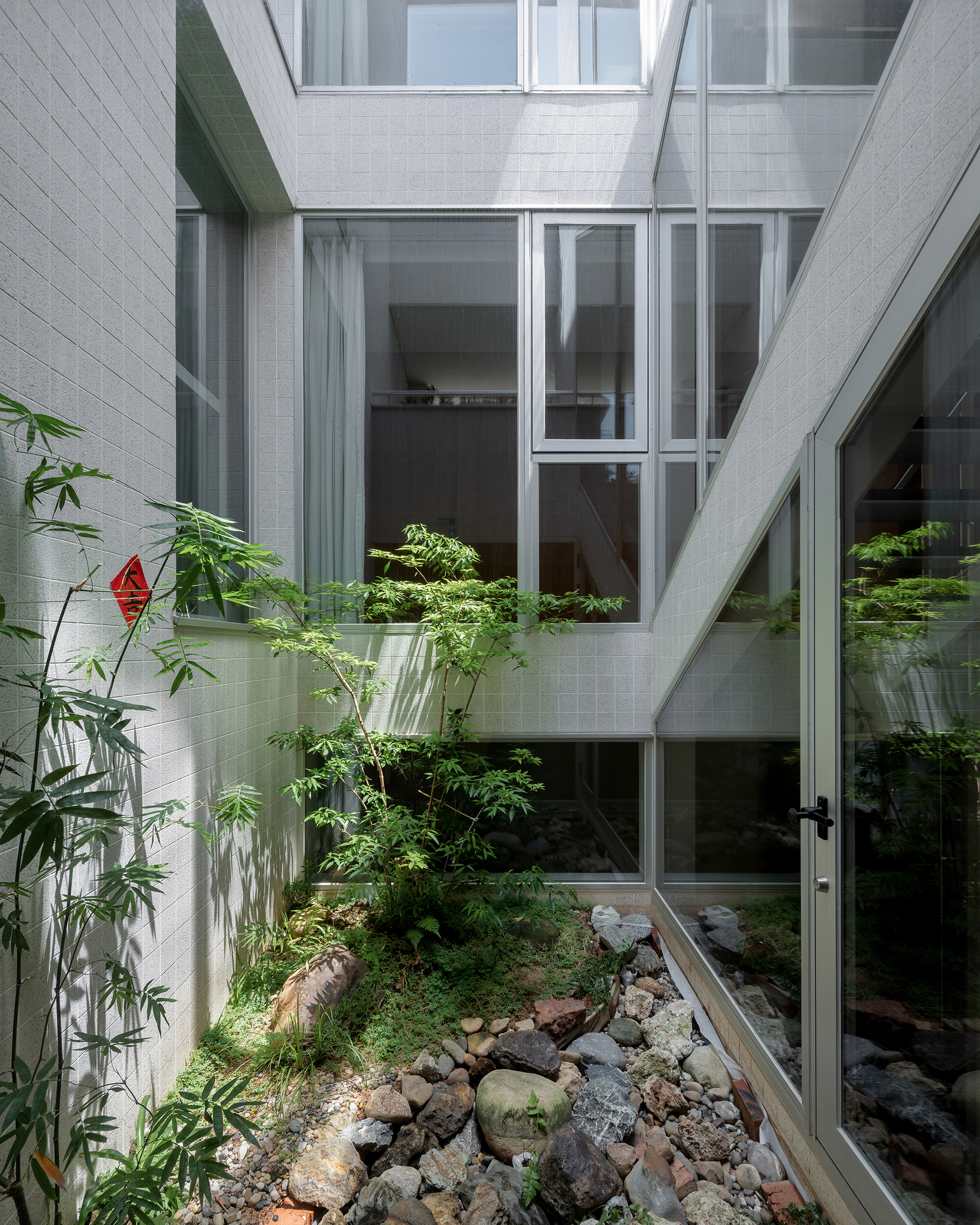 Interior courtyard with white tile walls, layered glazing, bamboo, and rock garden below