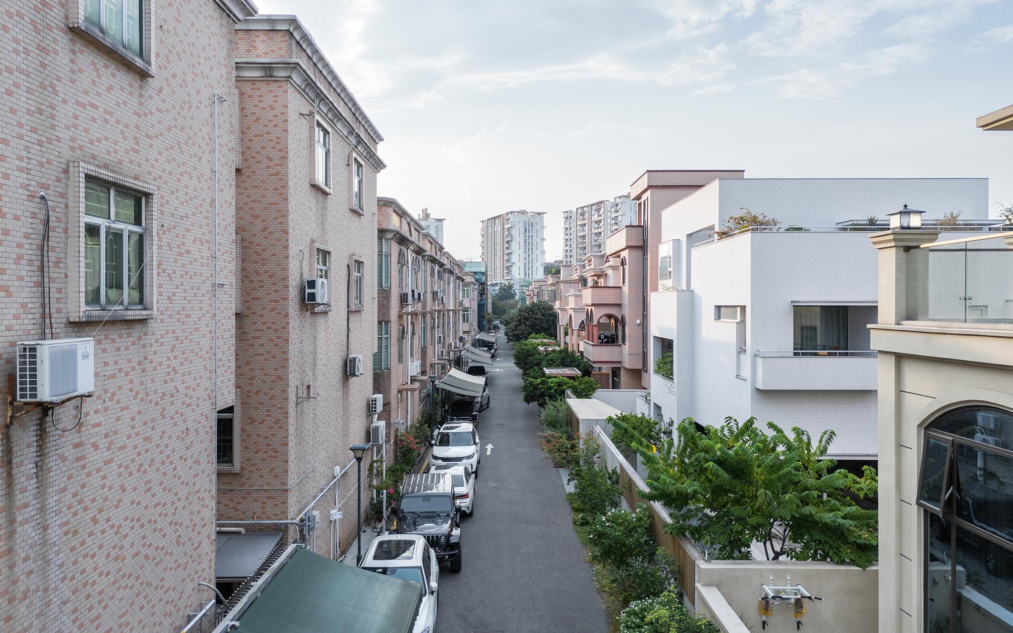 Street view between brick residential blocks with parked cars and green landscaping under cloudy skies