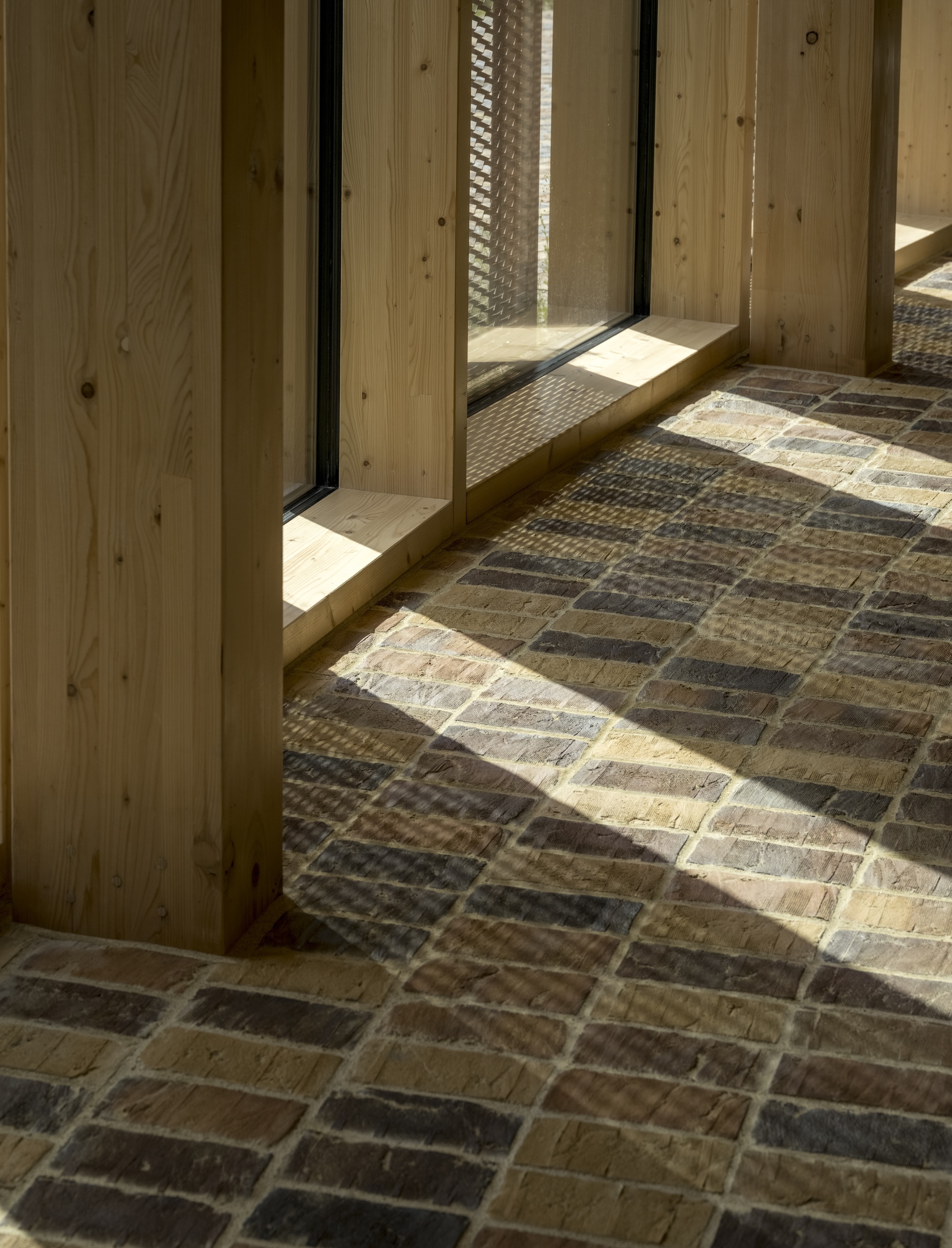 Sunlight casting shadows across multicolored brick floor at timber door threshold with mesh screen beyond
