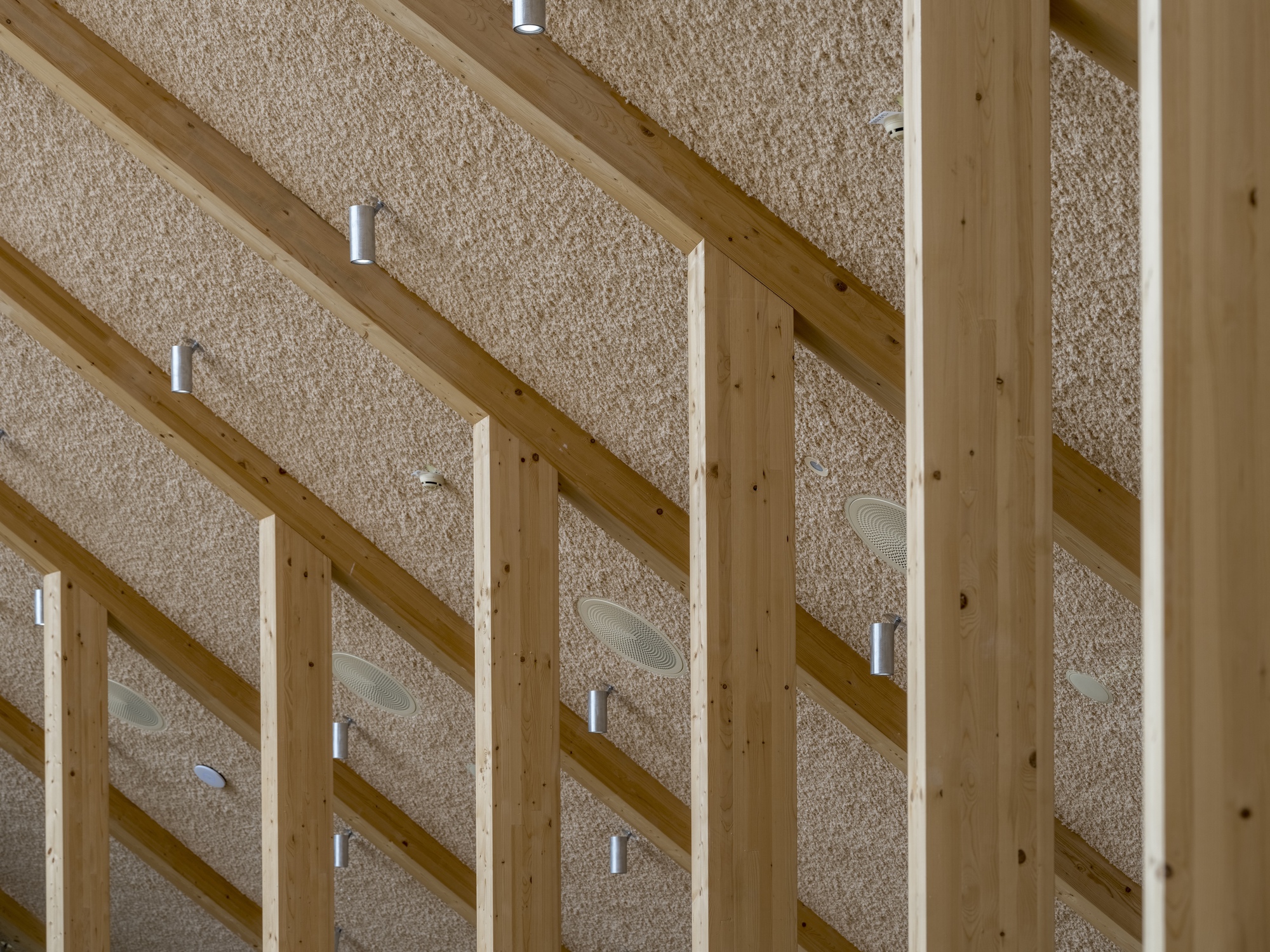 Upward view of exposed timber beams and textured ceiling panels with integrated cylindrical light fittings