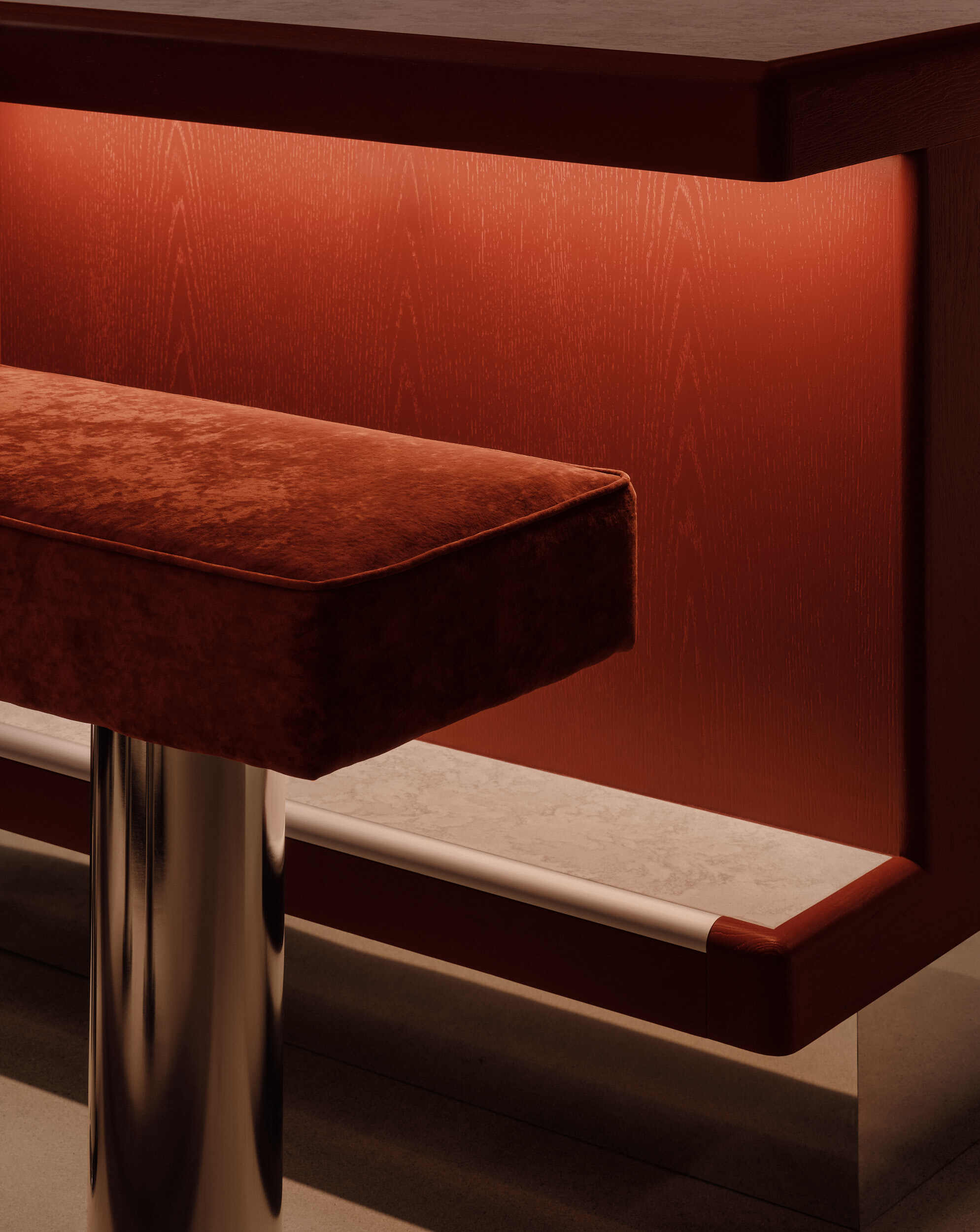 Banquette seating with rust-colored velvet upholstery and metal legs against a textured orange wall