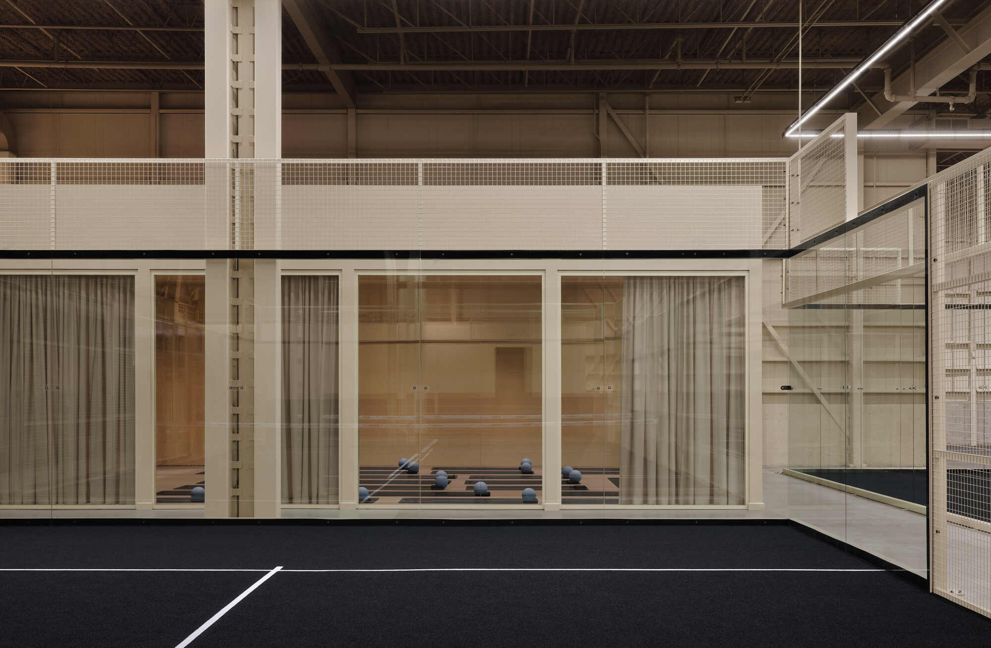 Interior sports court with glass-fronted viewing room, metal mesh partitions and exposed truss ceiling