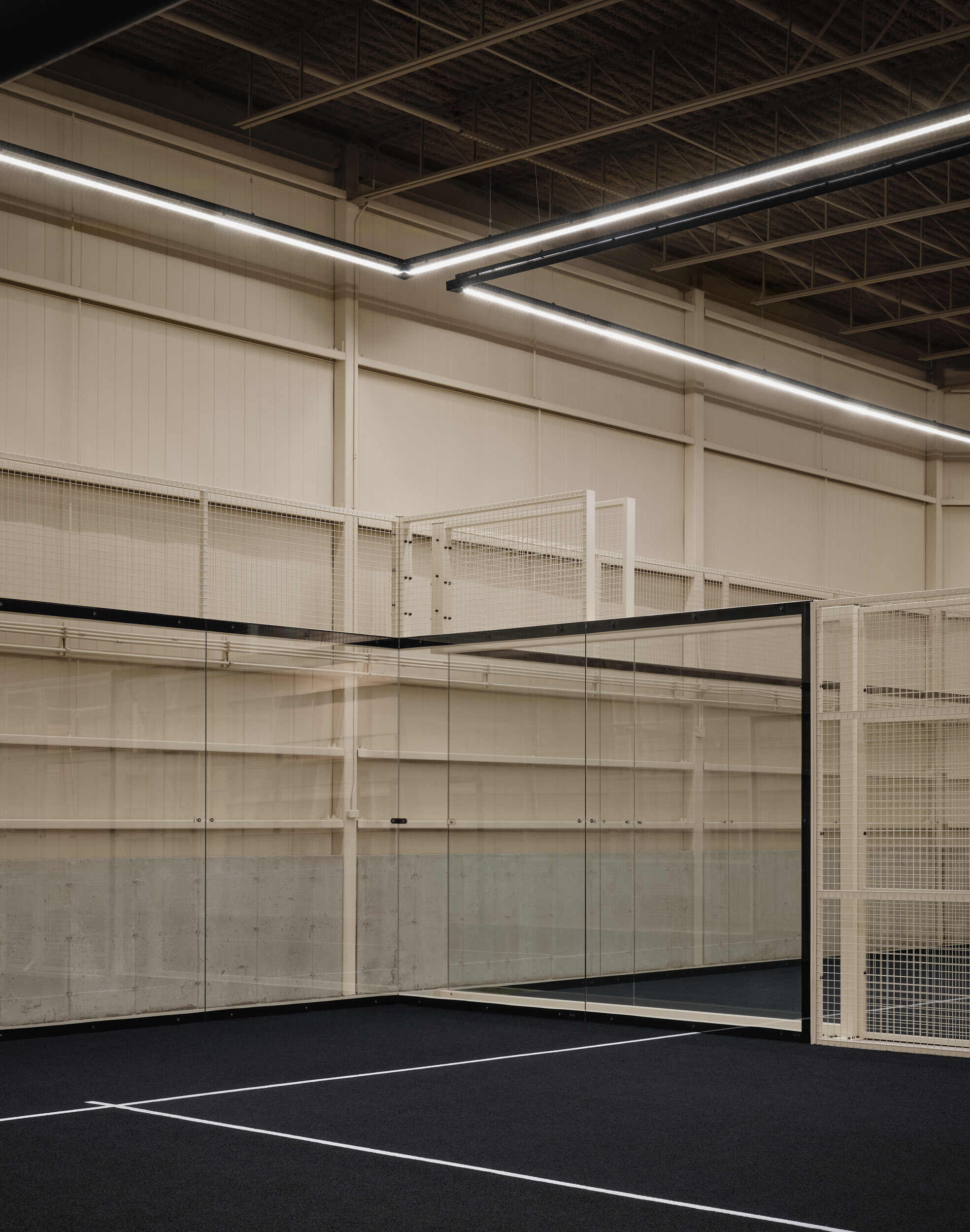 Corner of indoor court showing built-in storage shelving, wire mesh enclosure and linear lighting overhead