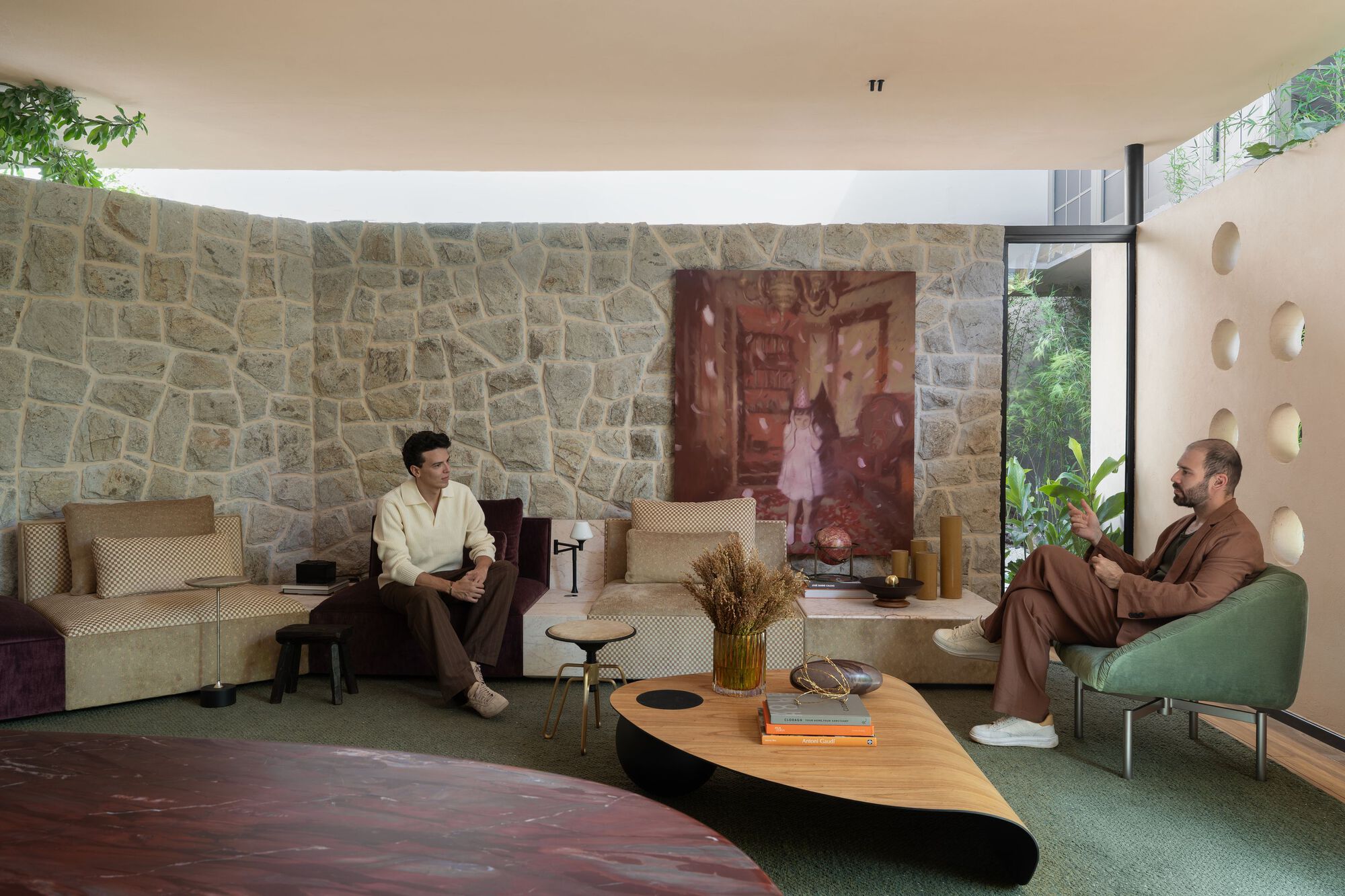 Curved stone wall with large artwork hung above low seating and two occupants in conversation