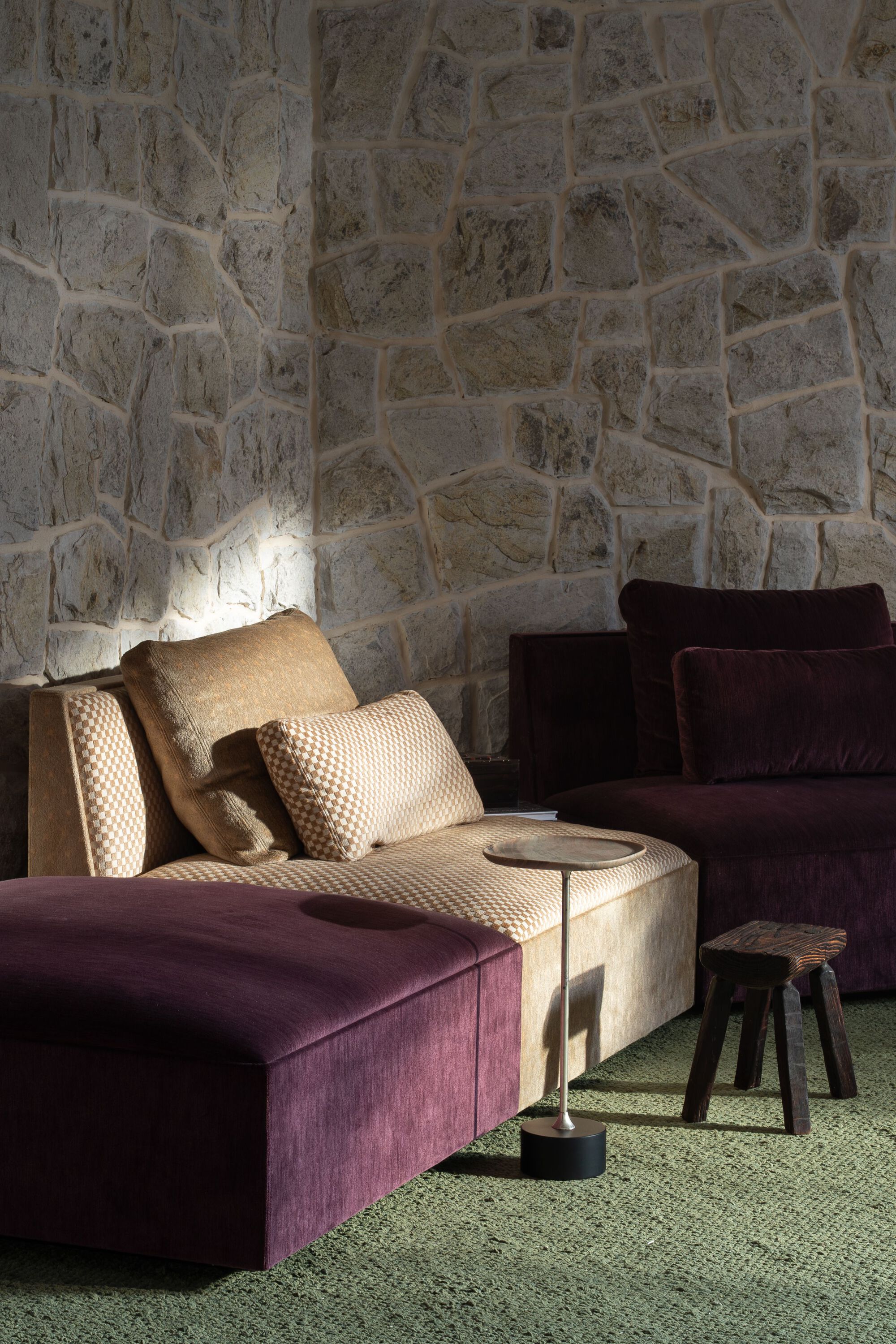 Seating area with velvet upholstered lounge chairs against an exposed stone wall with grazing light