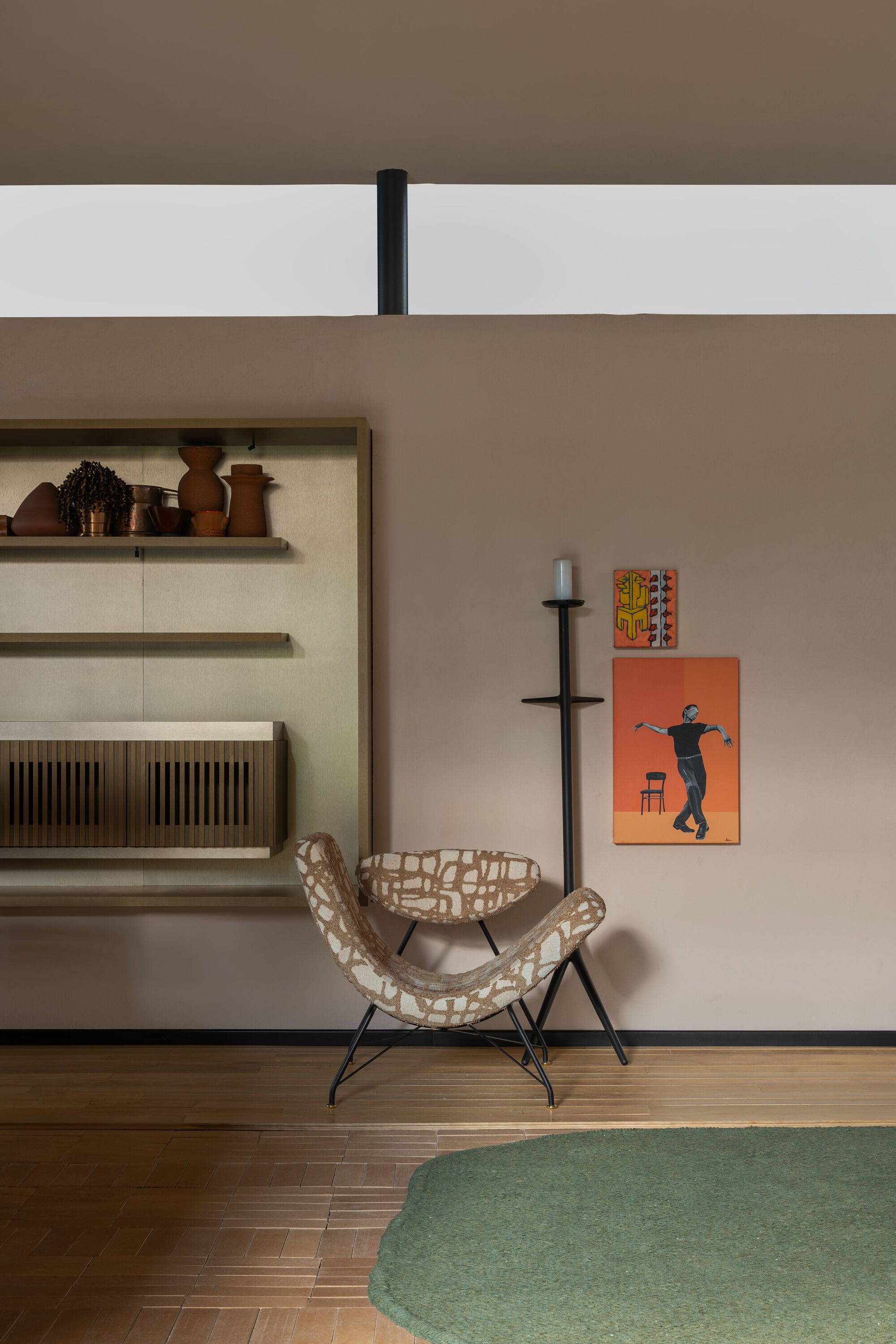 Woven lounge chair beside a black floor candelabra against a warm taupe wall