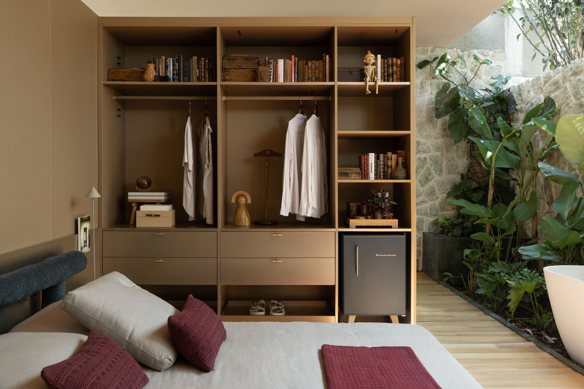 Open wardrobe unit with hanging garments and shelves beside a planted courtyard garden