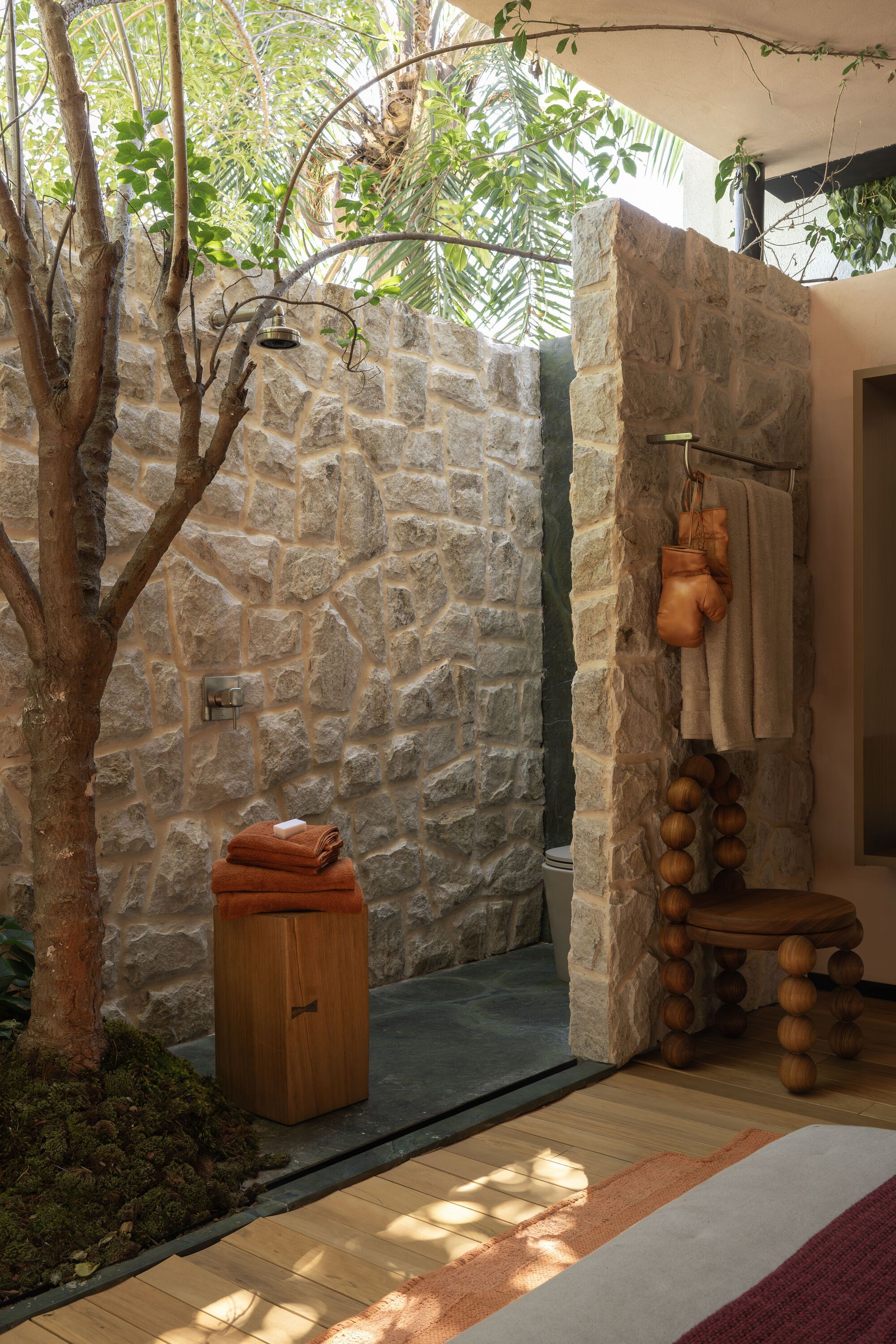 Open-air shower with rough stone walls and a tree growing through the space