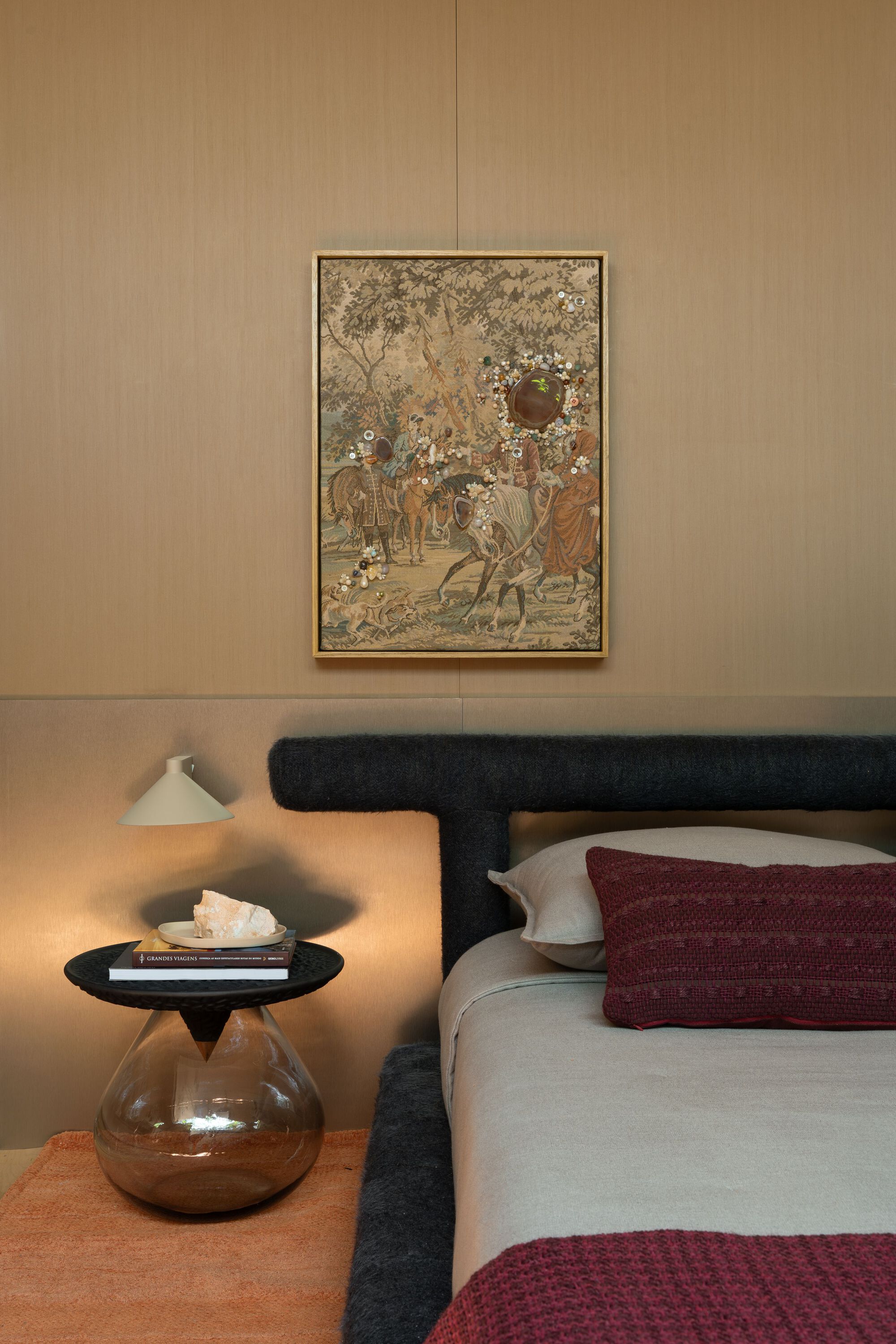 Bedroom with a framed tapestry above the headboard and a sculptural bedside table lamp