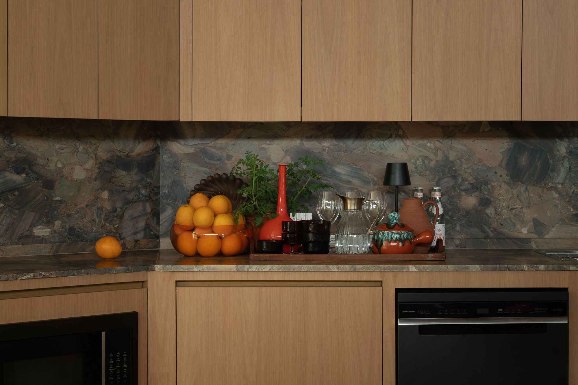 Kitchen counter with light wood cabinetry and multicolored stone backsplash beneath upper cabinets