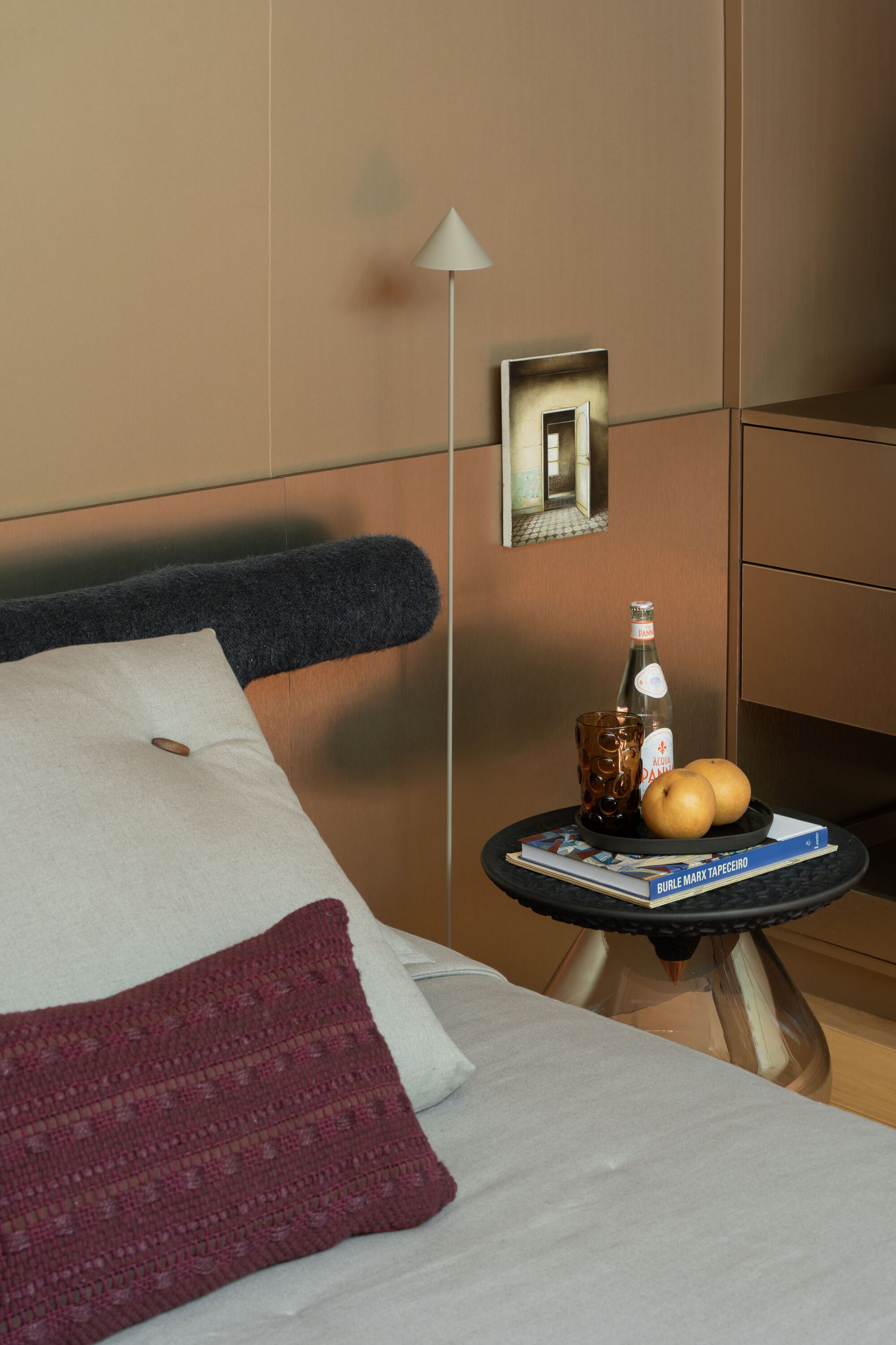 Bedside vignette with bronze mirror panel and conical floor lamp casting soft glow