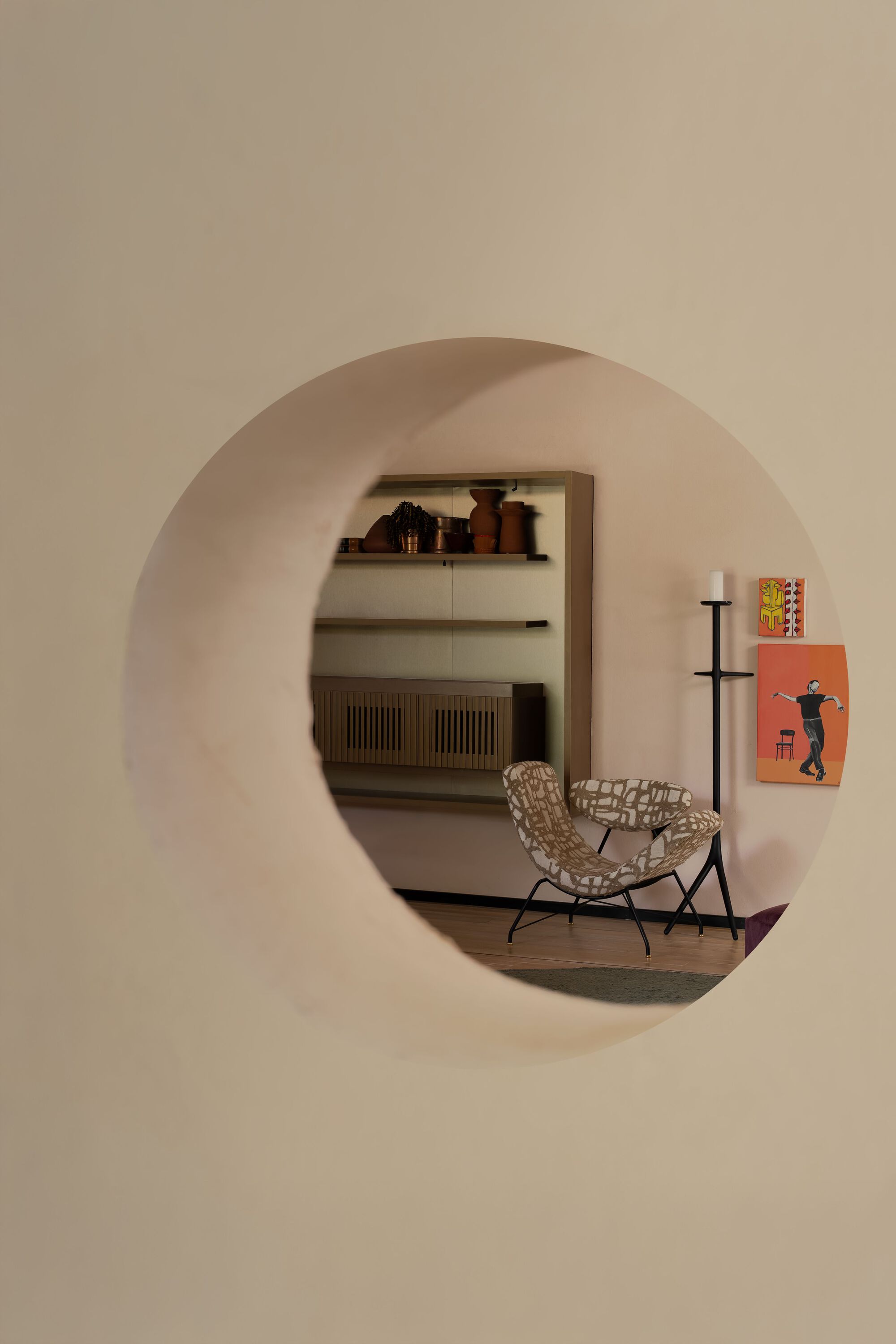 Circular wall opening framing a woven lounge chair and built-in storage beyond