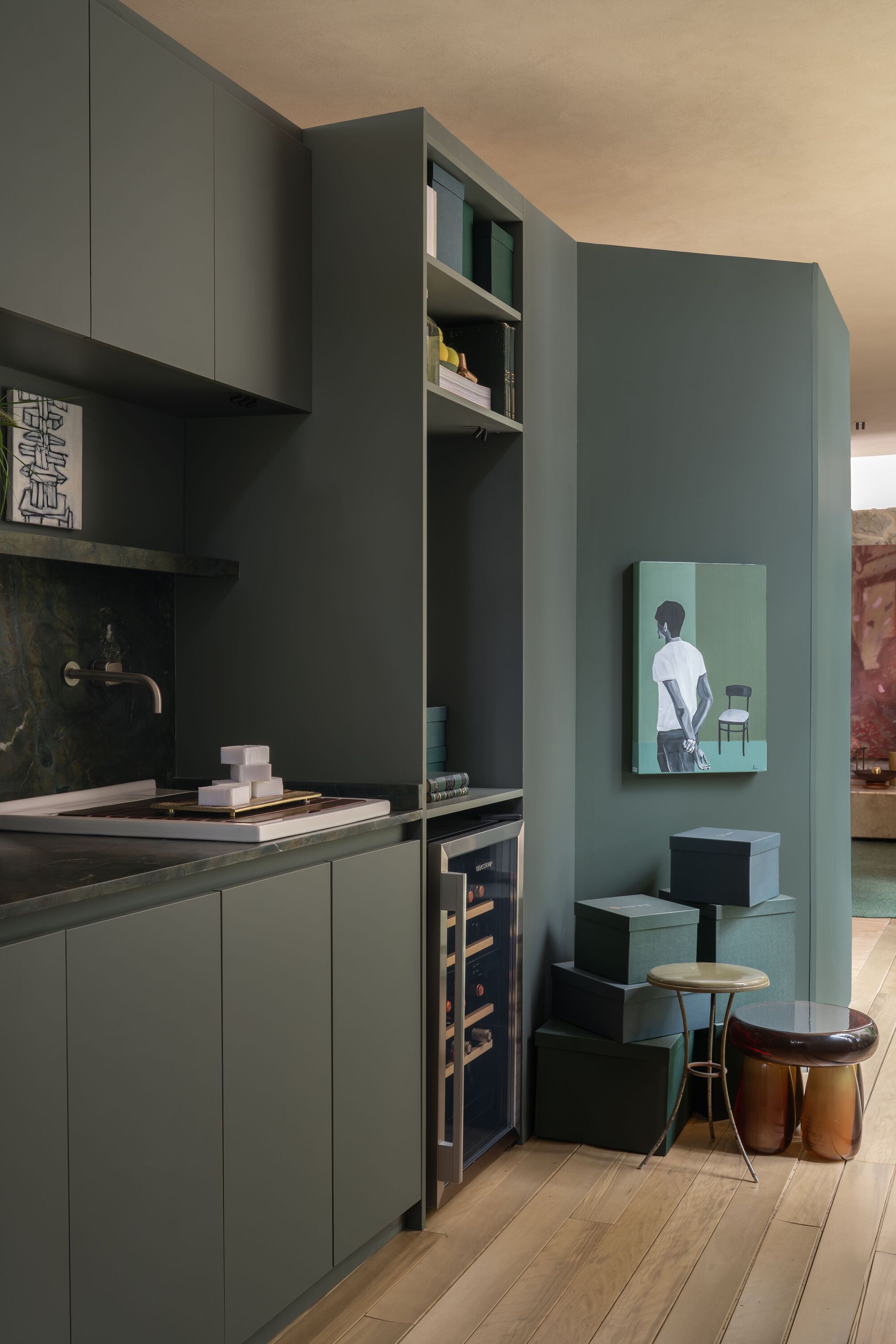 Sage green kitchen cabinetry with built-in wine cooler and open shelving beneath plywood ceiling