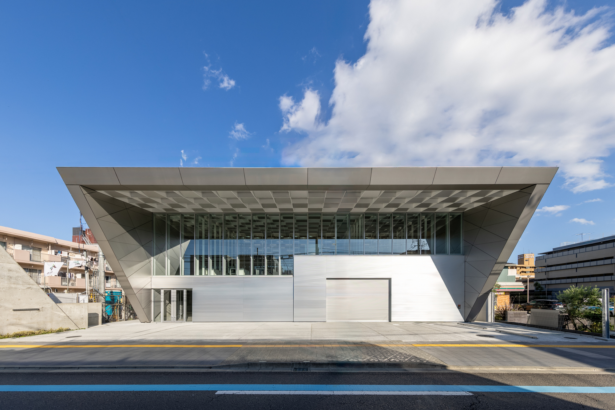 Street view of the angular white facade with deep cantilevered roof and full-height glazing under blue sky