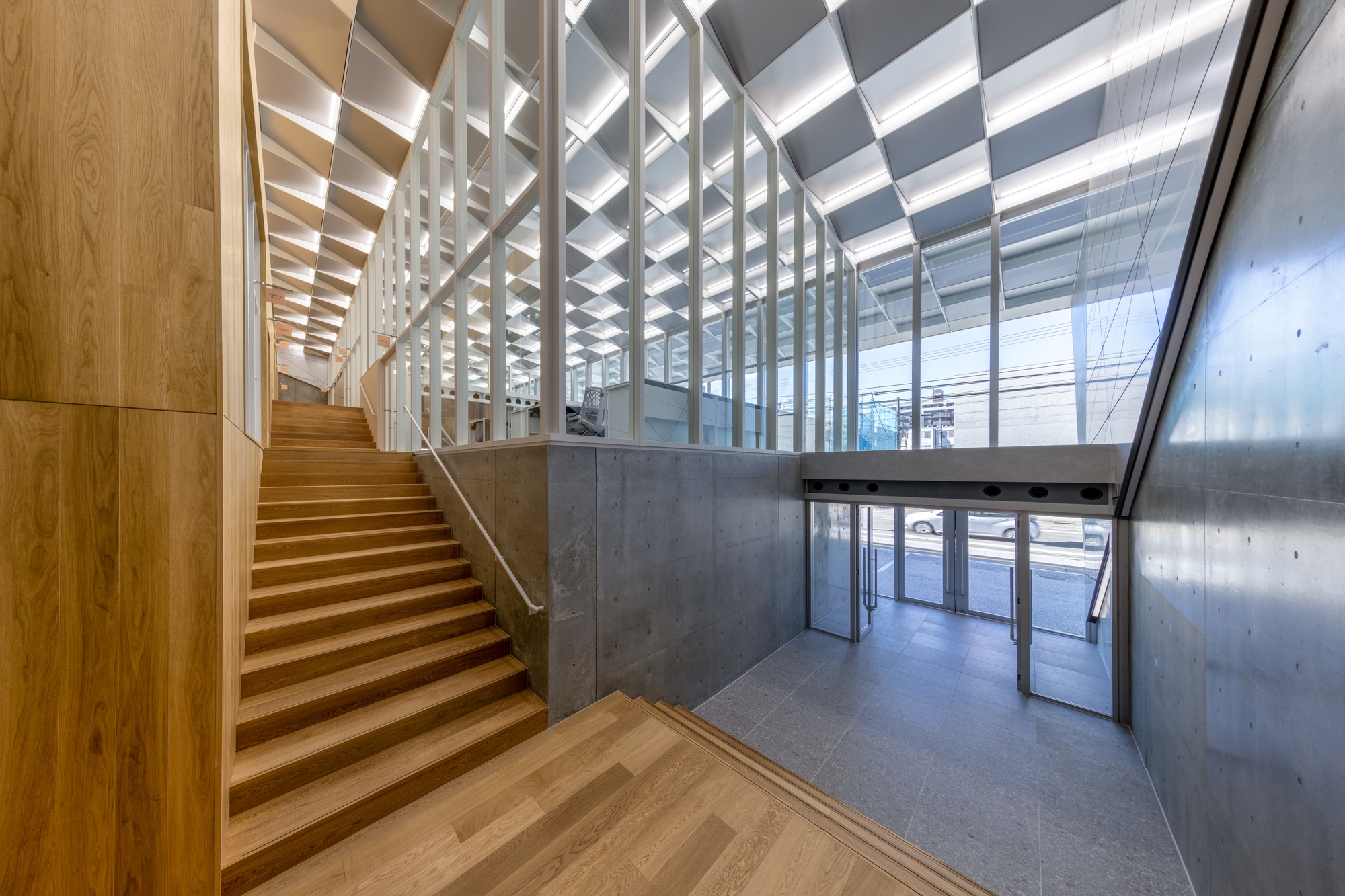 Timber staircase ascending from entry lobby with geometric ceiling coffers and concrete walls