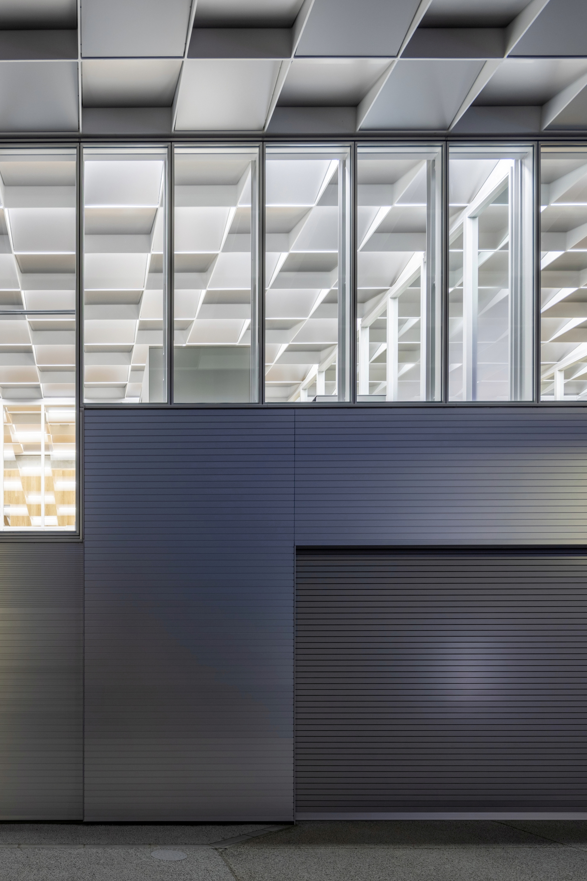 Exterior detail showing corrugated metal panels below glazing with geometric coffers above