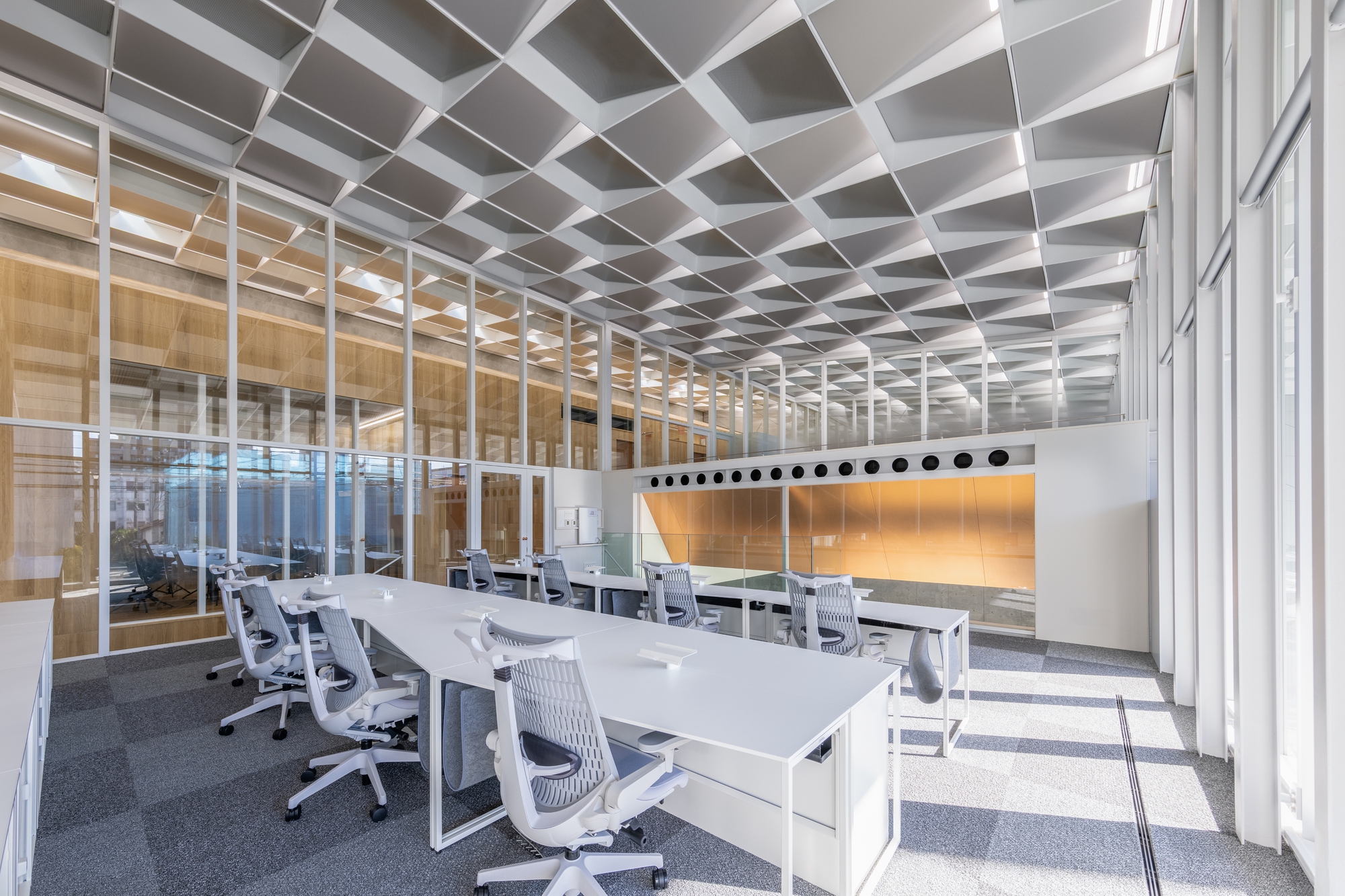 Open office workspace with white desks and chairs under a coffered ceiling grid with glass partitions