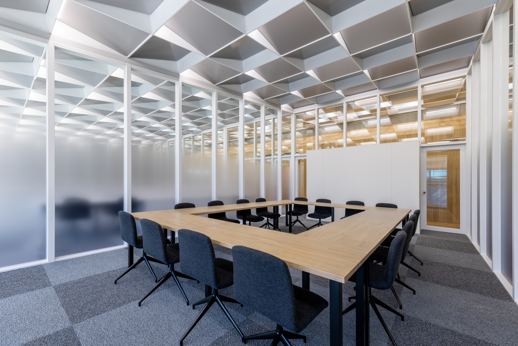 Conference room with wood table and chairs beneath a geometric coffered ceiling with frosted glass walls