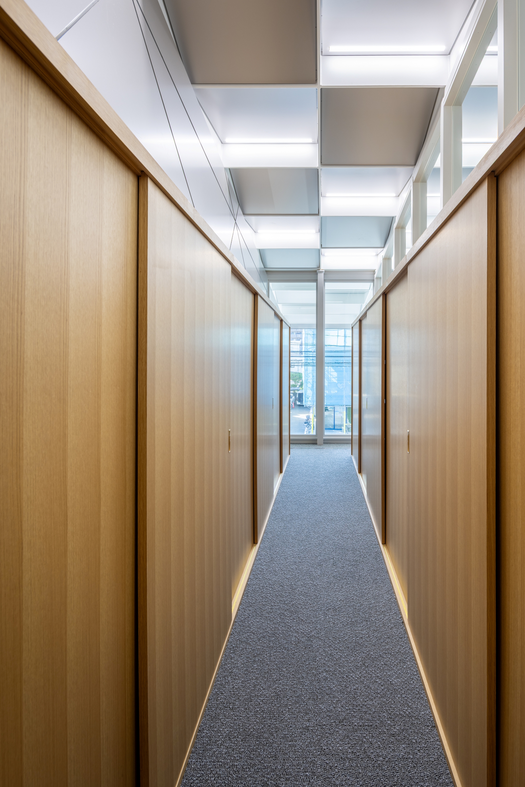 Hallway view with wood veneer wall panels and strip lighting beneath alternating white and grey ceiling coffers