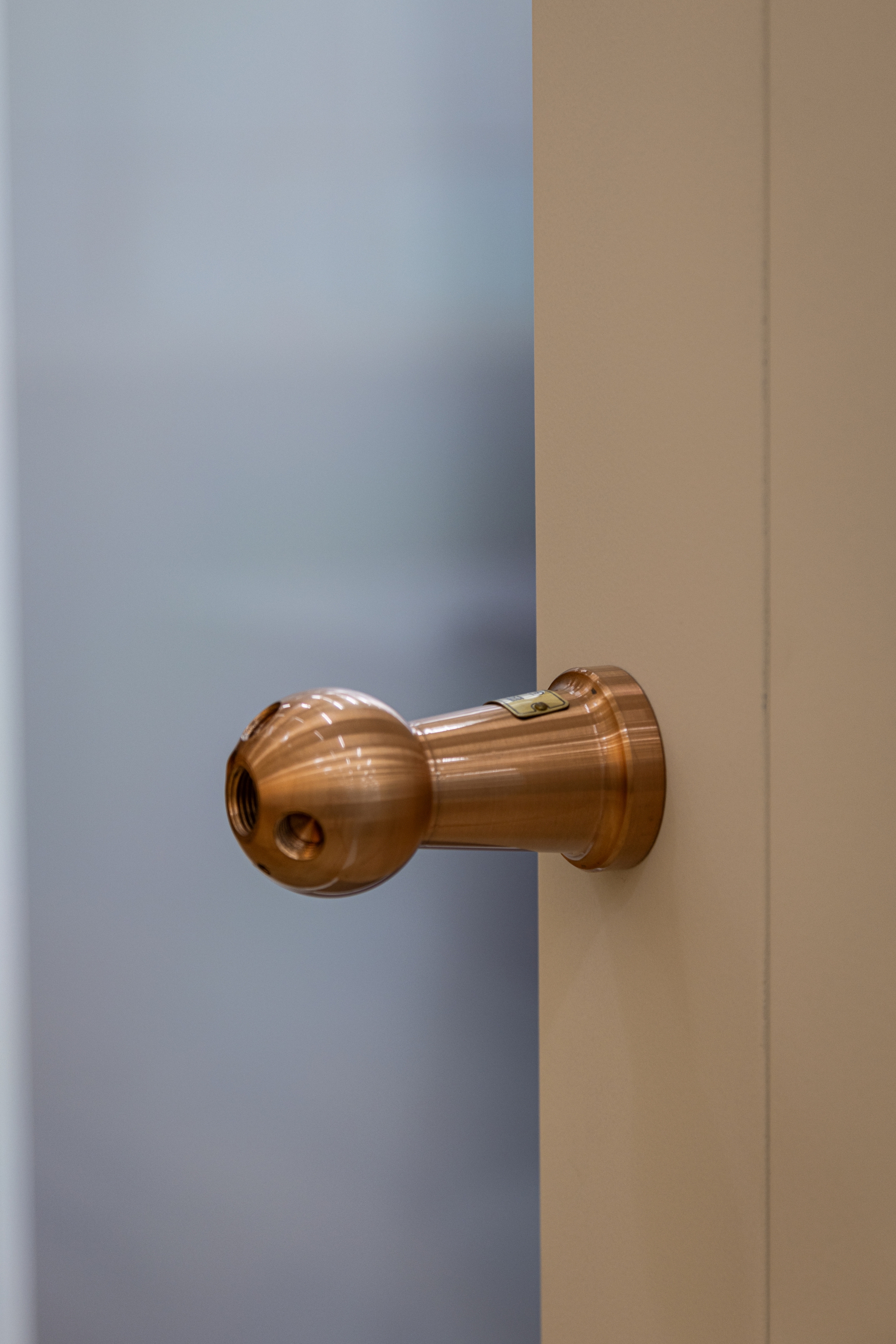 Polished copper door handle mounted on wood veneer door next to frosted glass panel