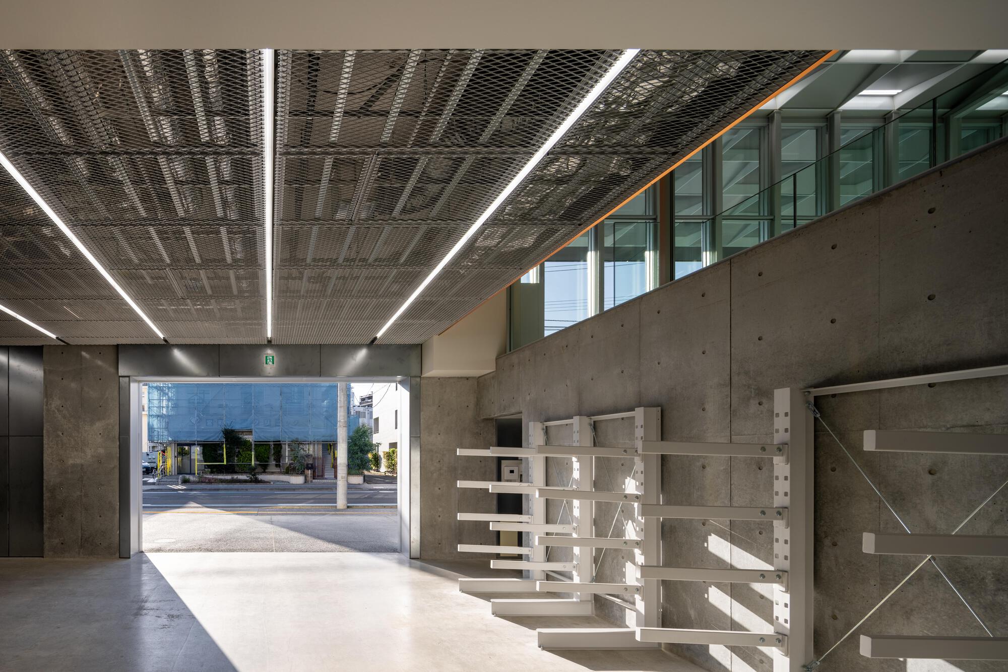 Ground floor lobby with exposed concrete walls and perforated metal ceiling under linear lighting