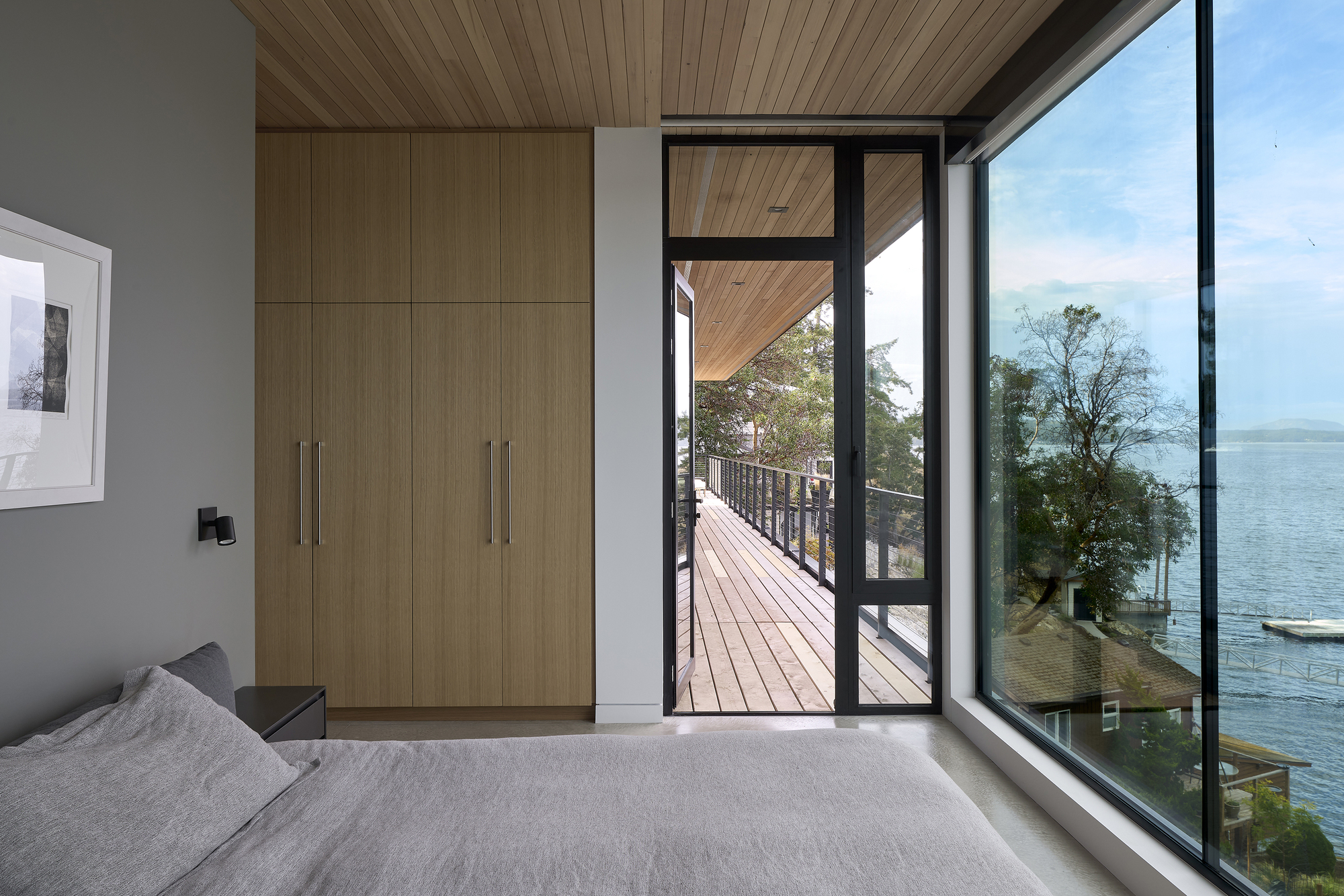 Bedroom with wood storage wall, glazed door opening to a timber deck with lake view