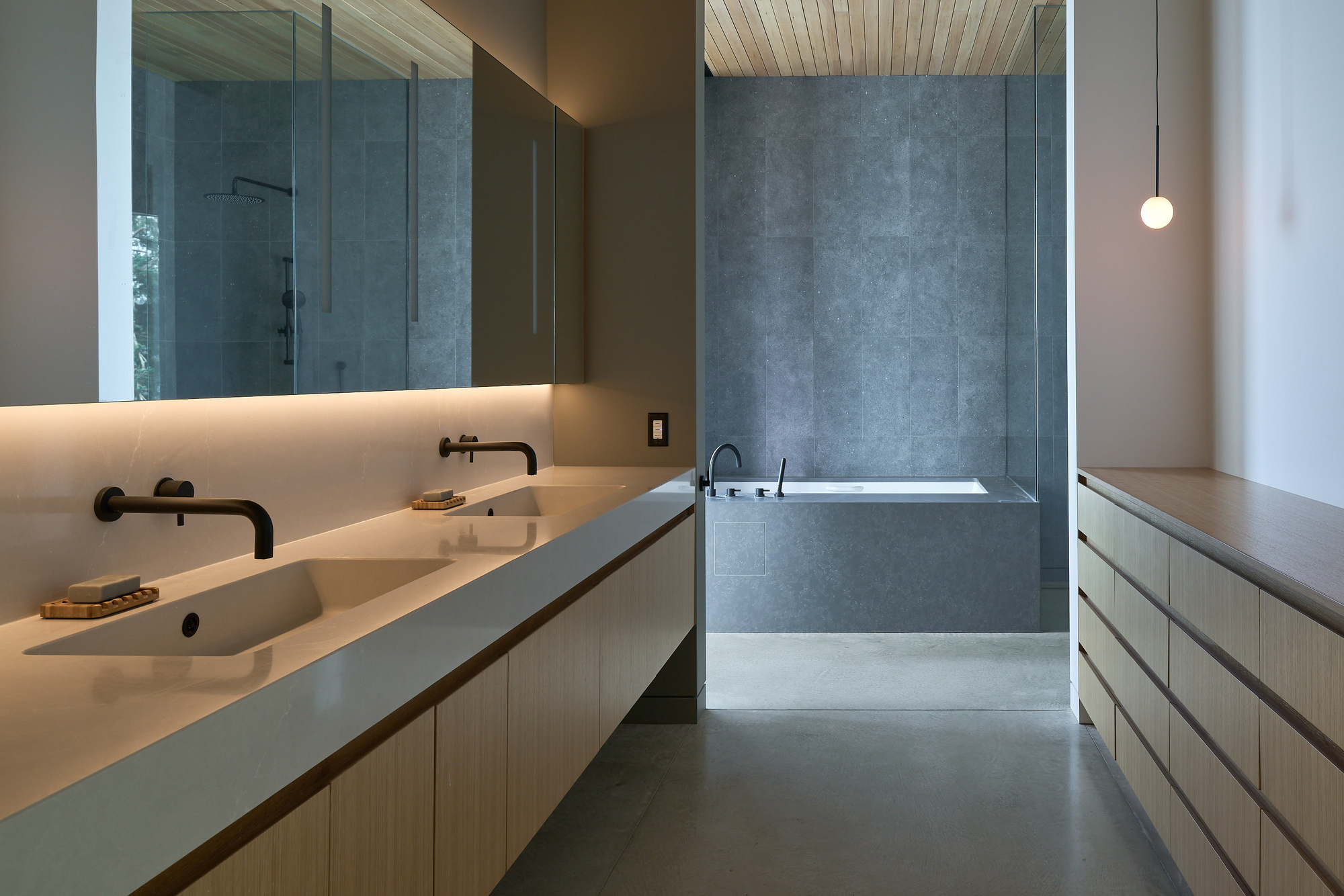 Bathroom with concrete double vanity, black fixtures, and grey plaster walls under a timber ceiling