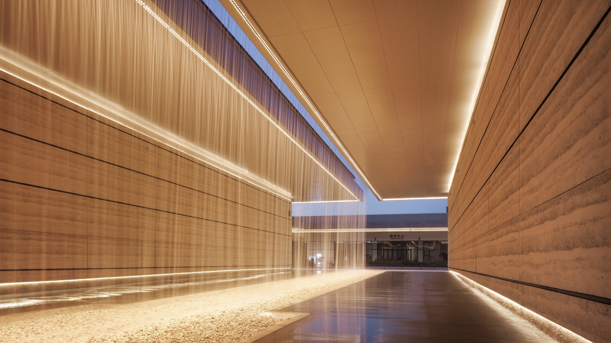 Interior corridor with glowing linear ceiling lights and bronze mesh wall panels at dusk