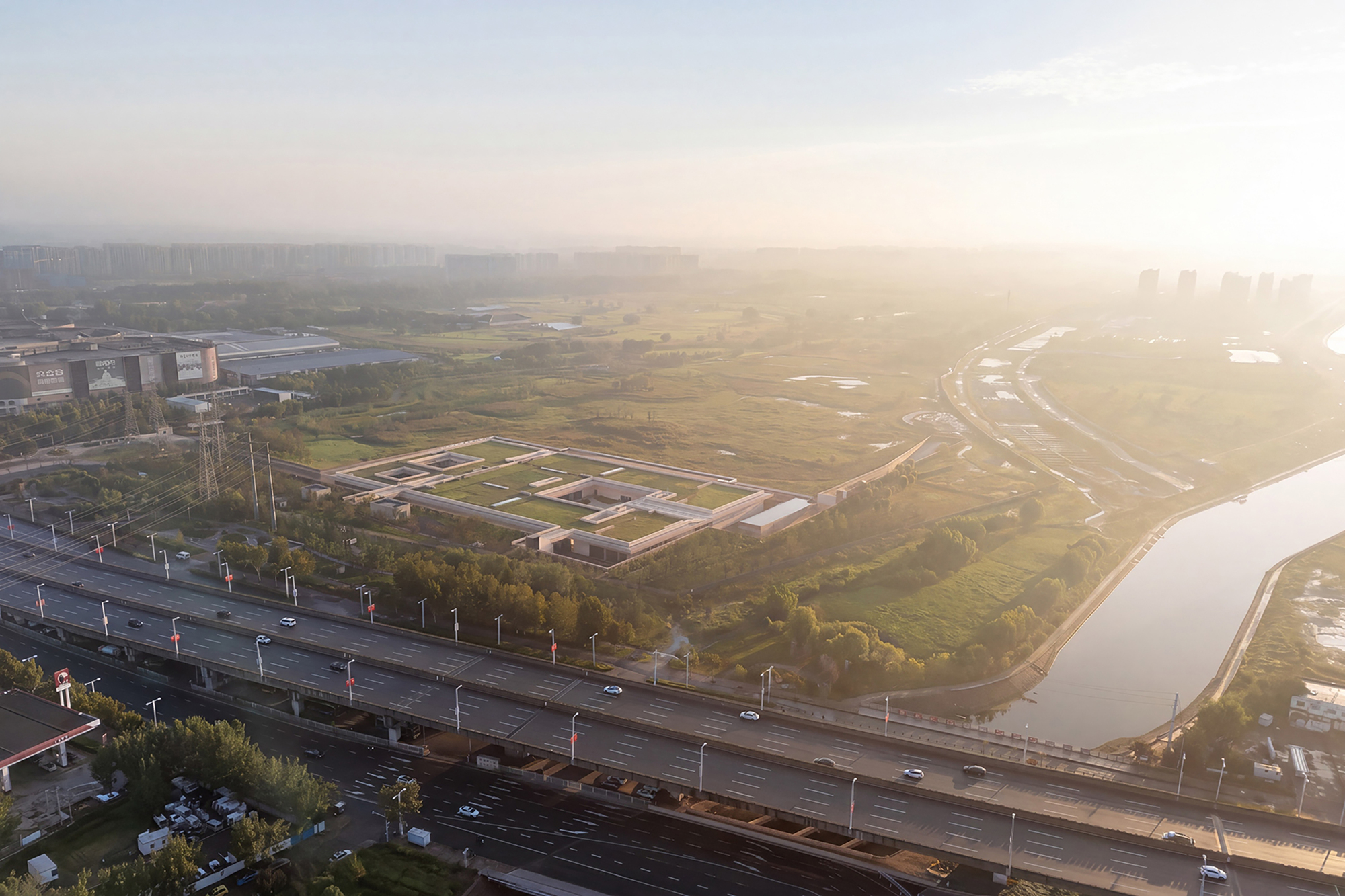 Aerial view of a walled compound with nested courtyards set in open grassland near a highway at sunrise