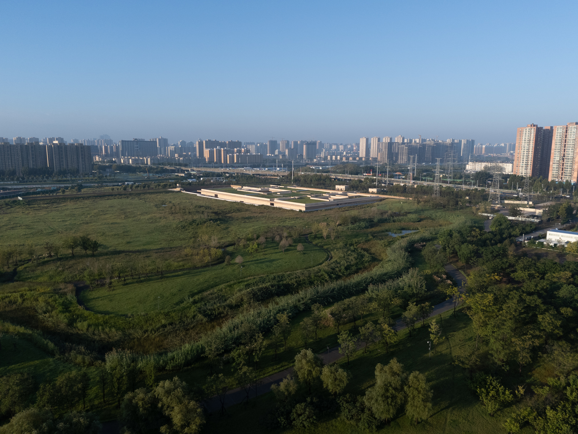 Distant view of the horizontal complex surrounded by planted berms and trees with residential towers beyond