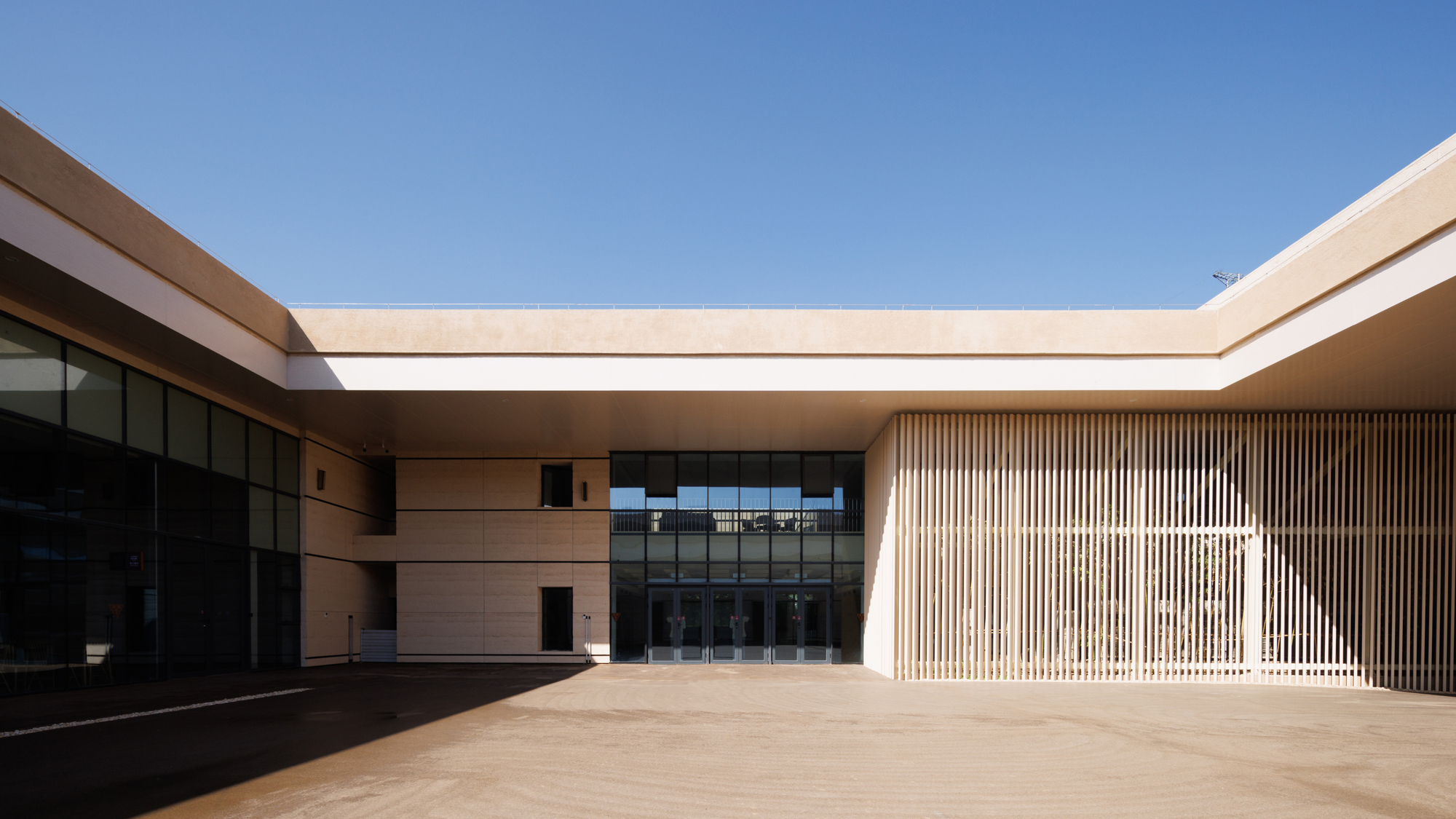 Open courtyard with vertical timber screen wall and dark glass facade under blue sky