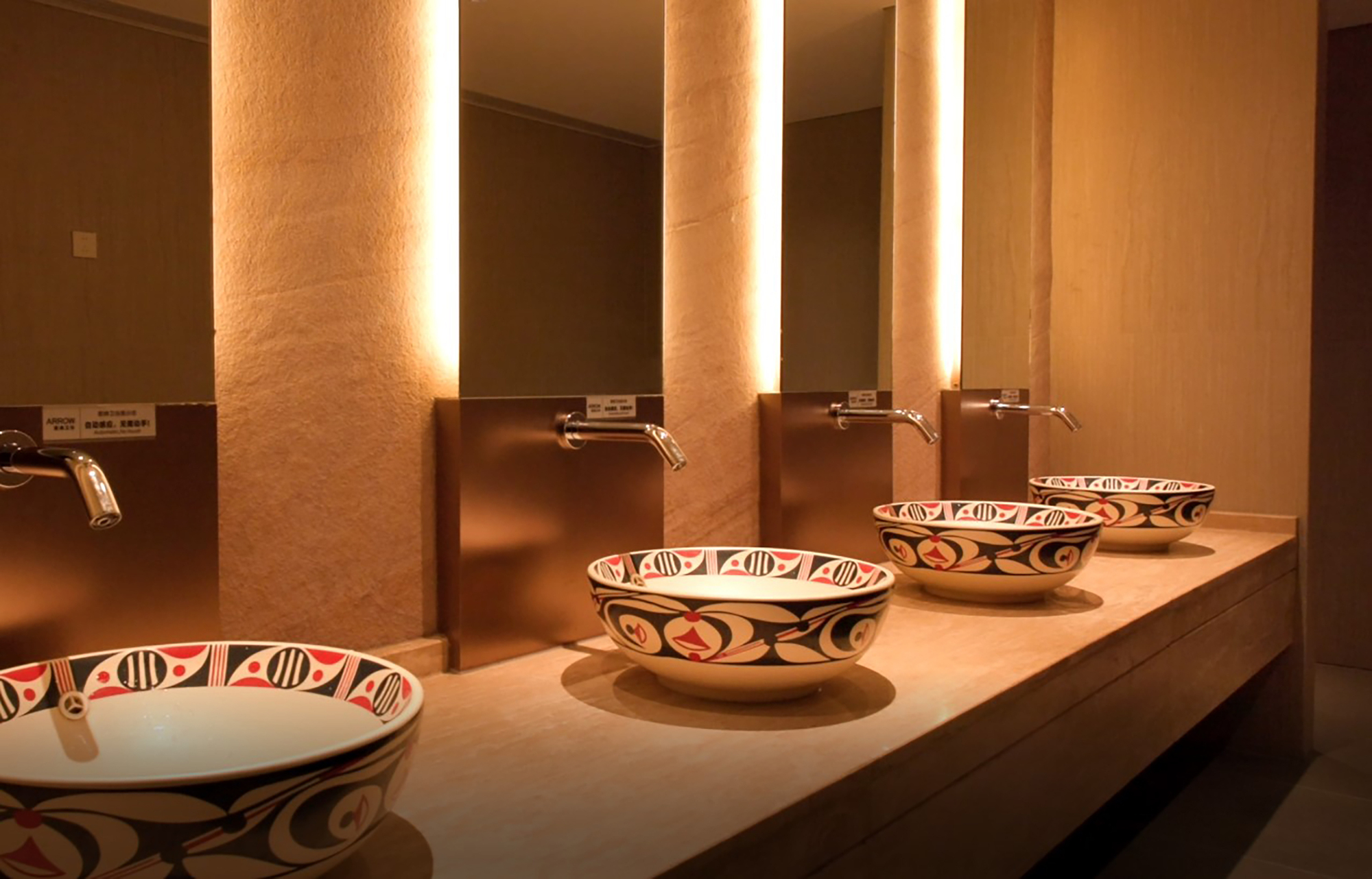 Washroom counter with handpainted ceramic basins and vertically-lit textured wall behind wall-mounted faucets