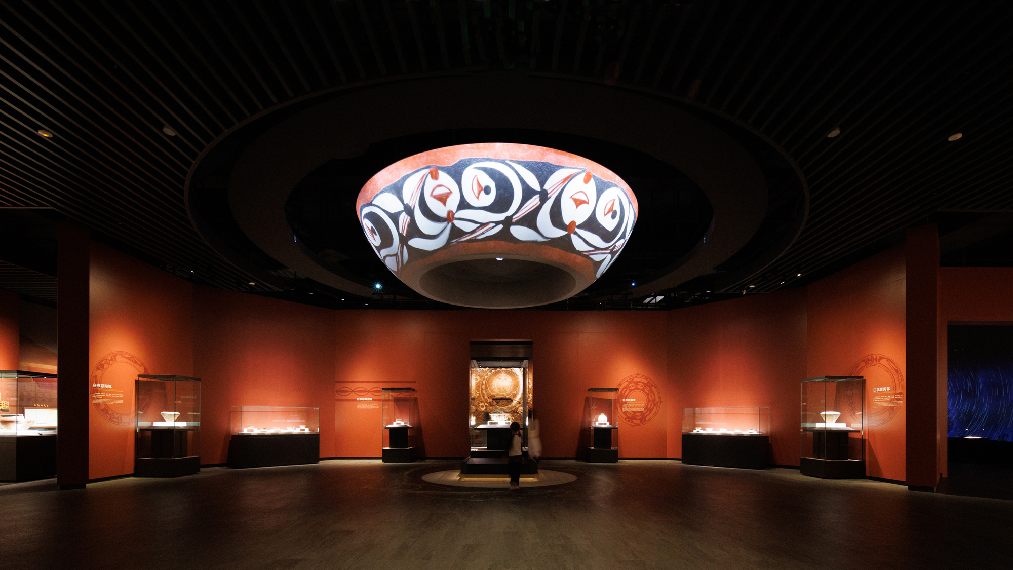 Gallery space with circular soffit displaying patterned textile beneath a dark slatted ceiling