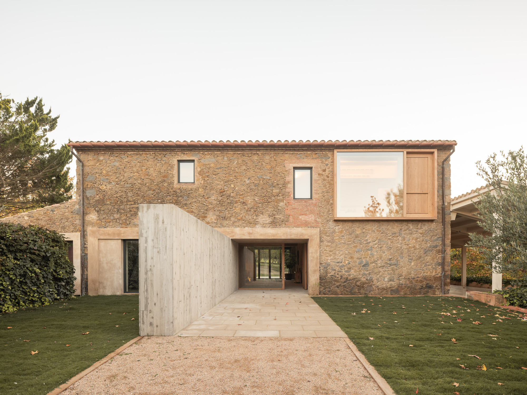 Stone facade with terracotta tile roof and timber-screened entryway under an overcast sky