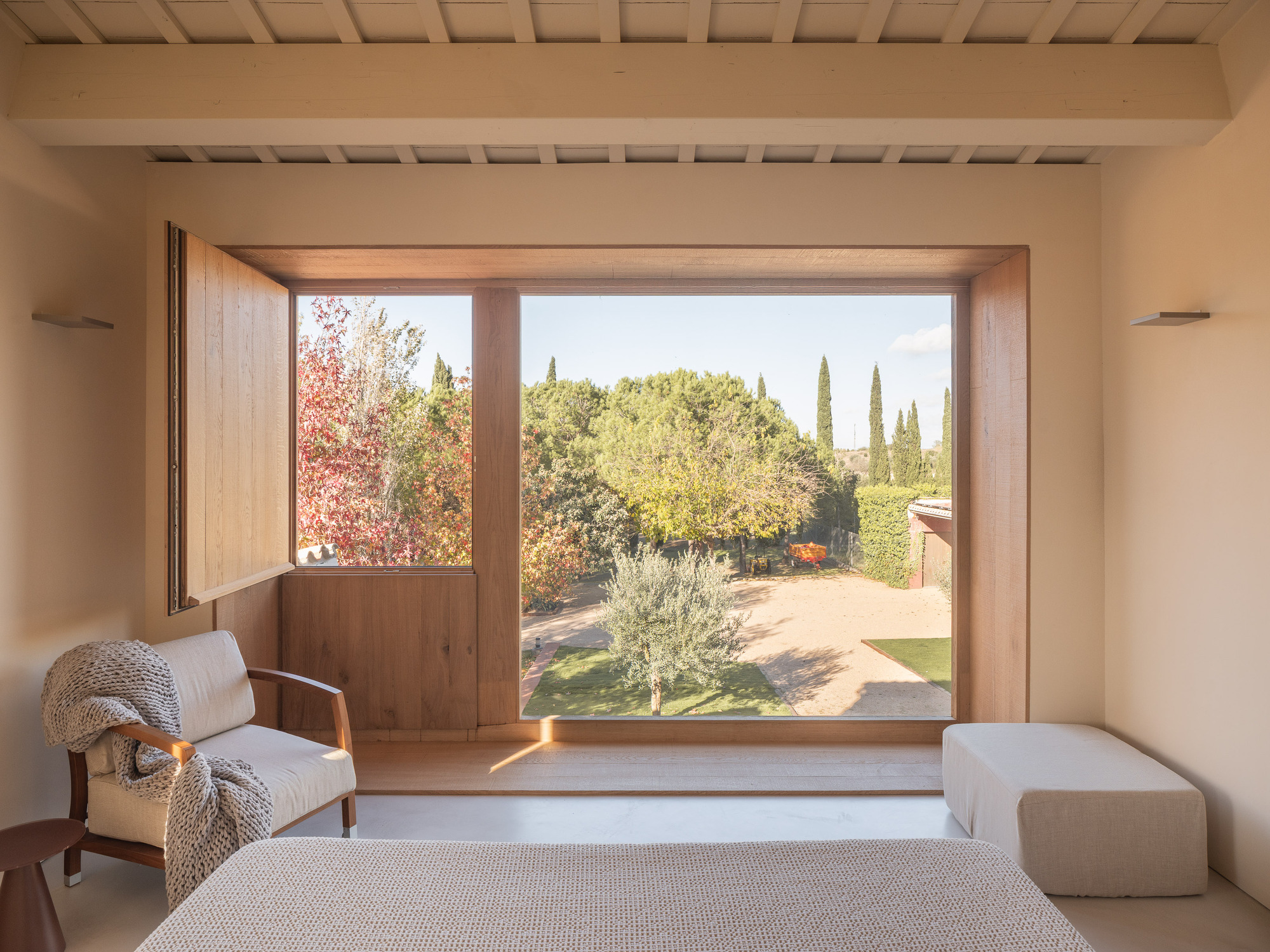 Timber-framed window alcove framing a view of olive trees and autumn foliage in the garden
